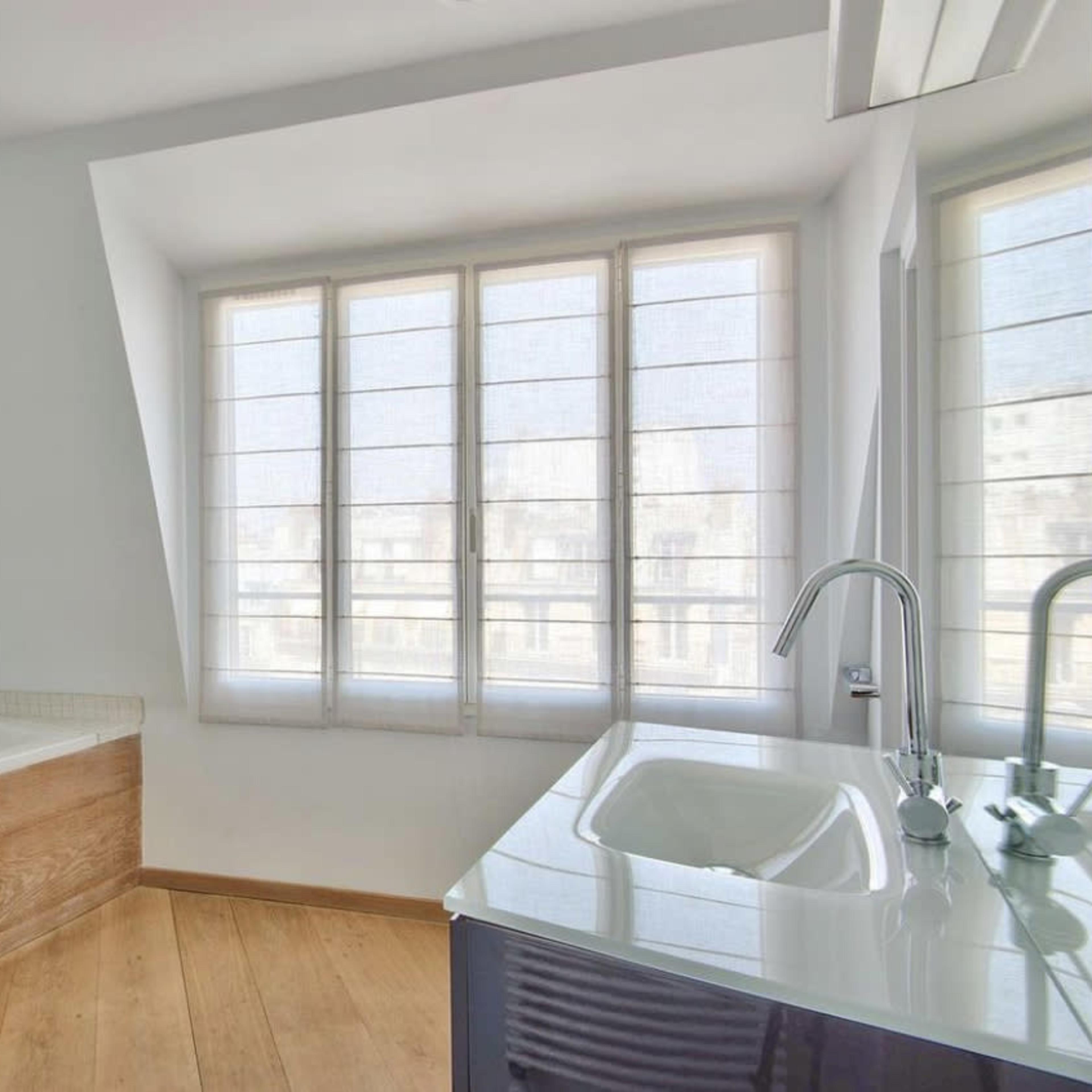A modern bathroom featuring a bathtub, a sink with a modern faucet, and large windows allowing natural light to enter.