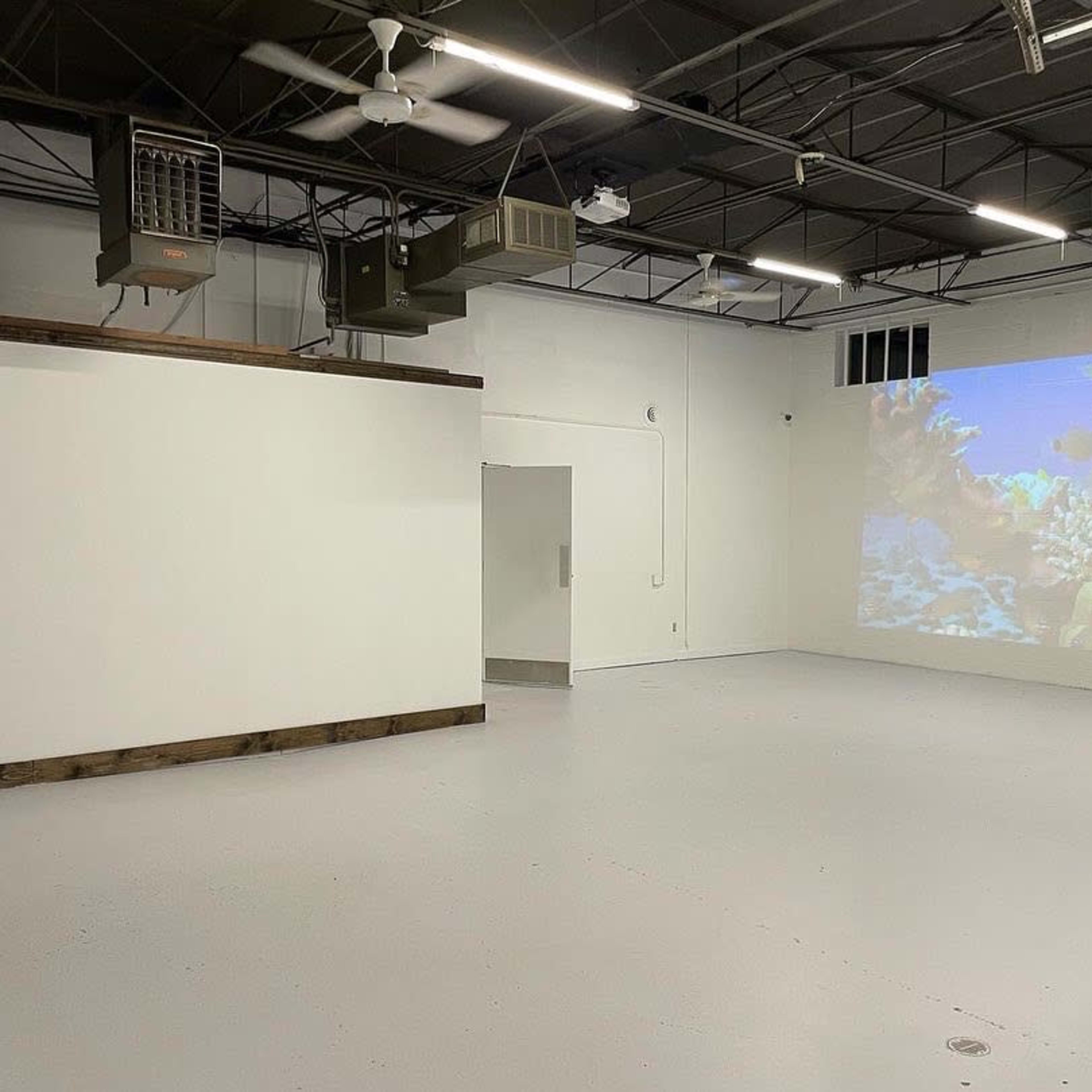 An empty room with a smooth white floor, a projection of a coral reef scene on one wall, and ventilation units mounted on the ceiling.