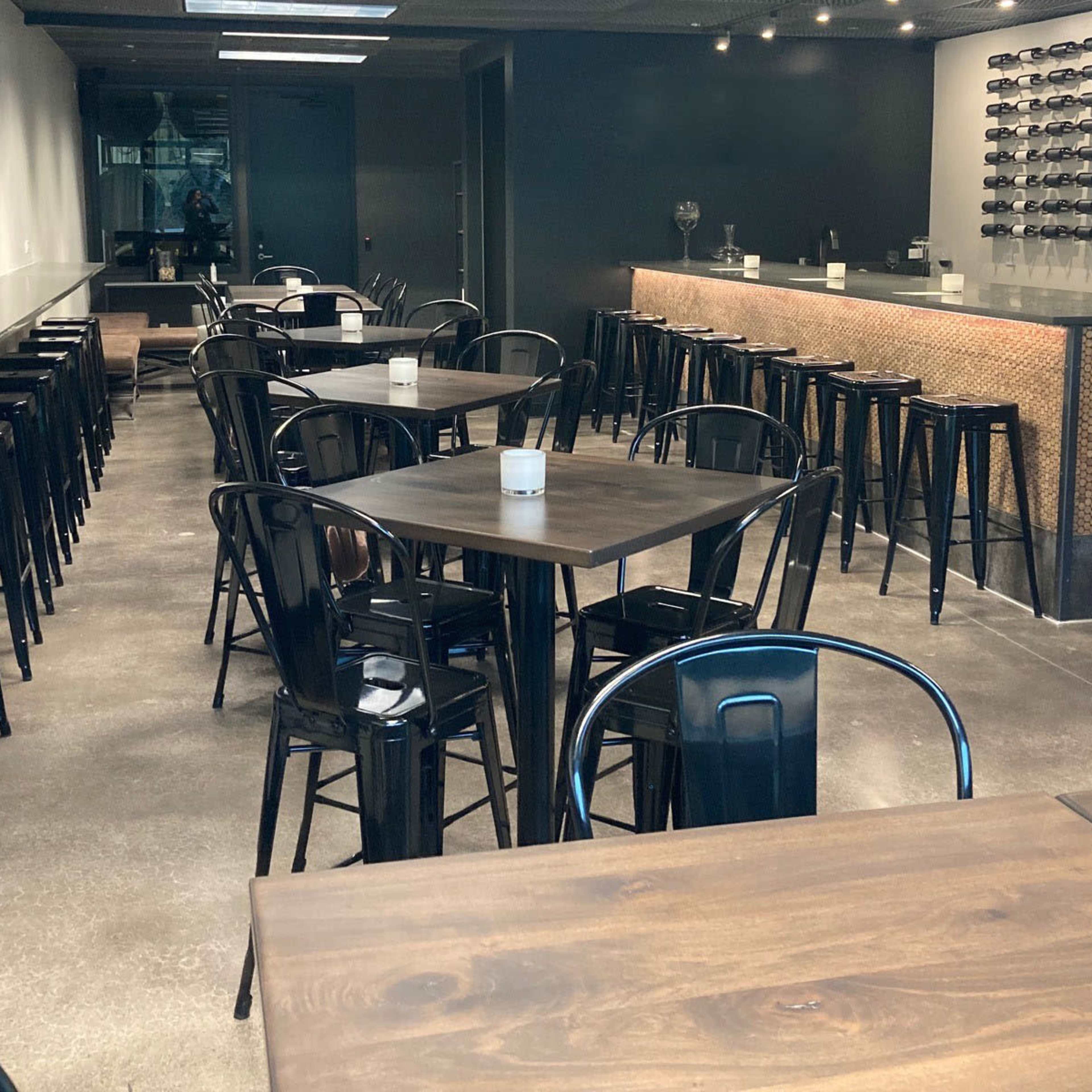A modern bar and dining area with several wooden tables and black metal stools arranged neatly along the walls.