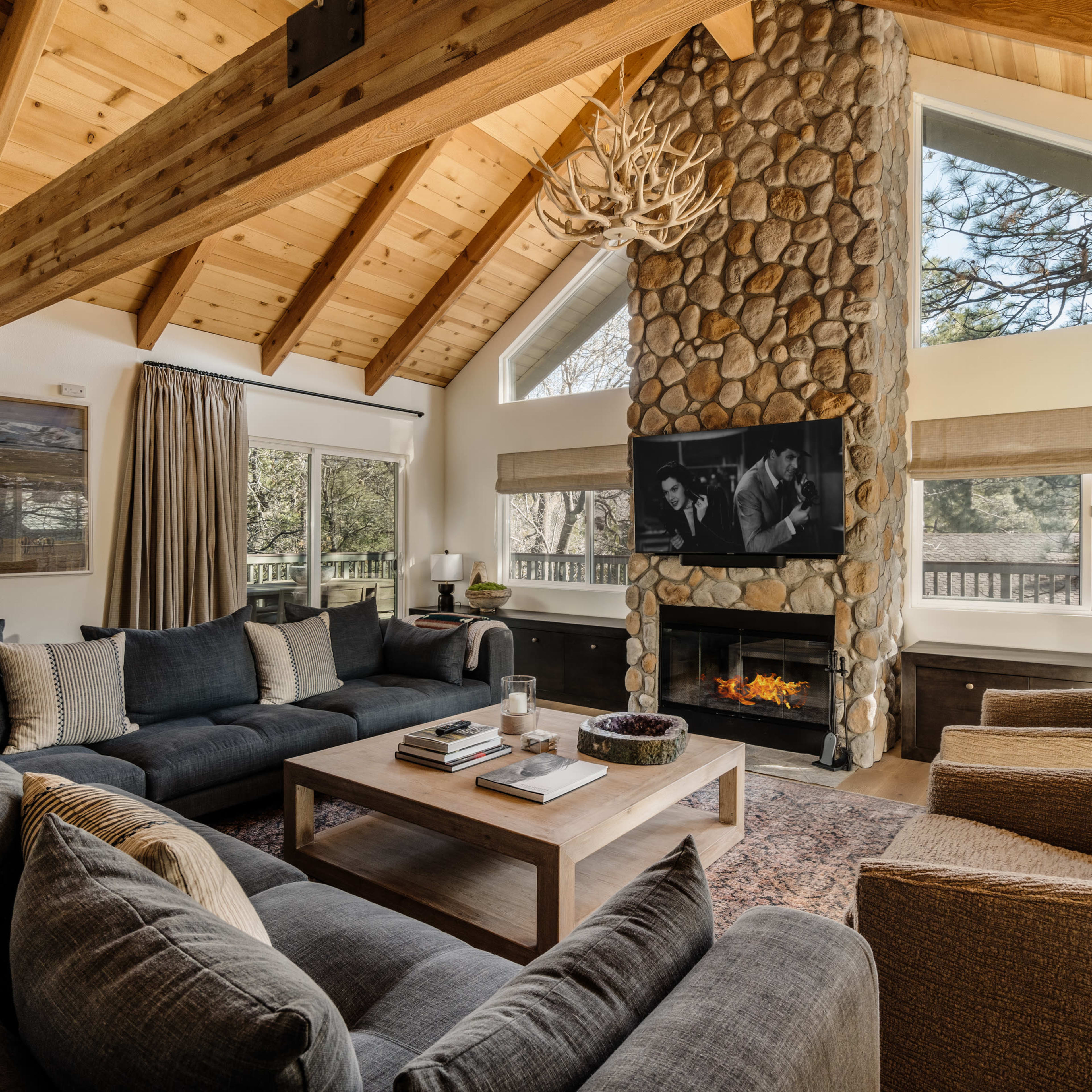 The living room features a large stone fireplace, vaulted wooden ceilings, and a sectional sofa arranged around a coffee table.