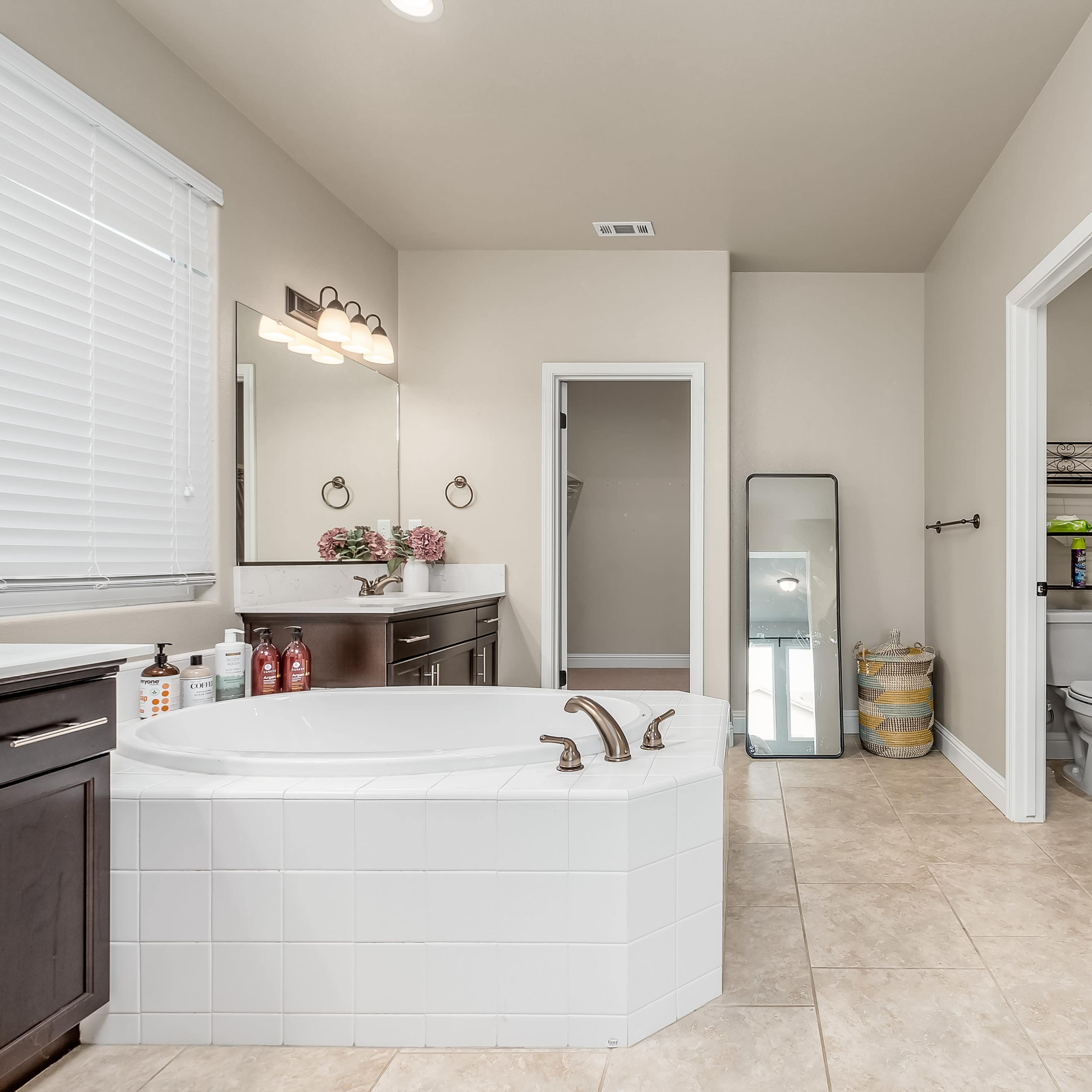 A spacious bathroom featuring a freestanding bathtub, a glass-enclosed shower, a double vanity, and a mirror leaning against the wall.