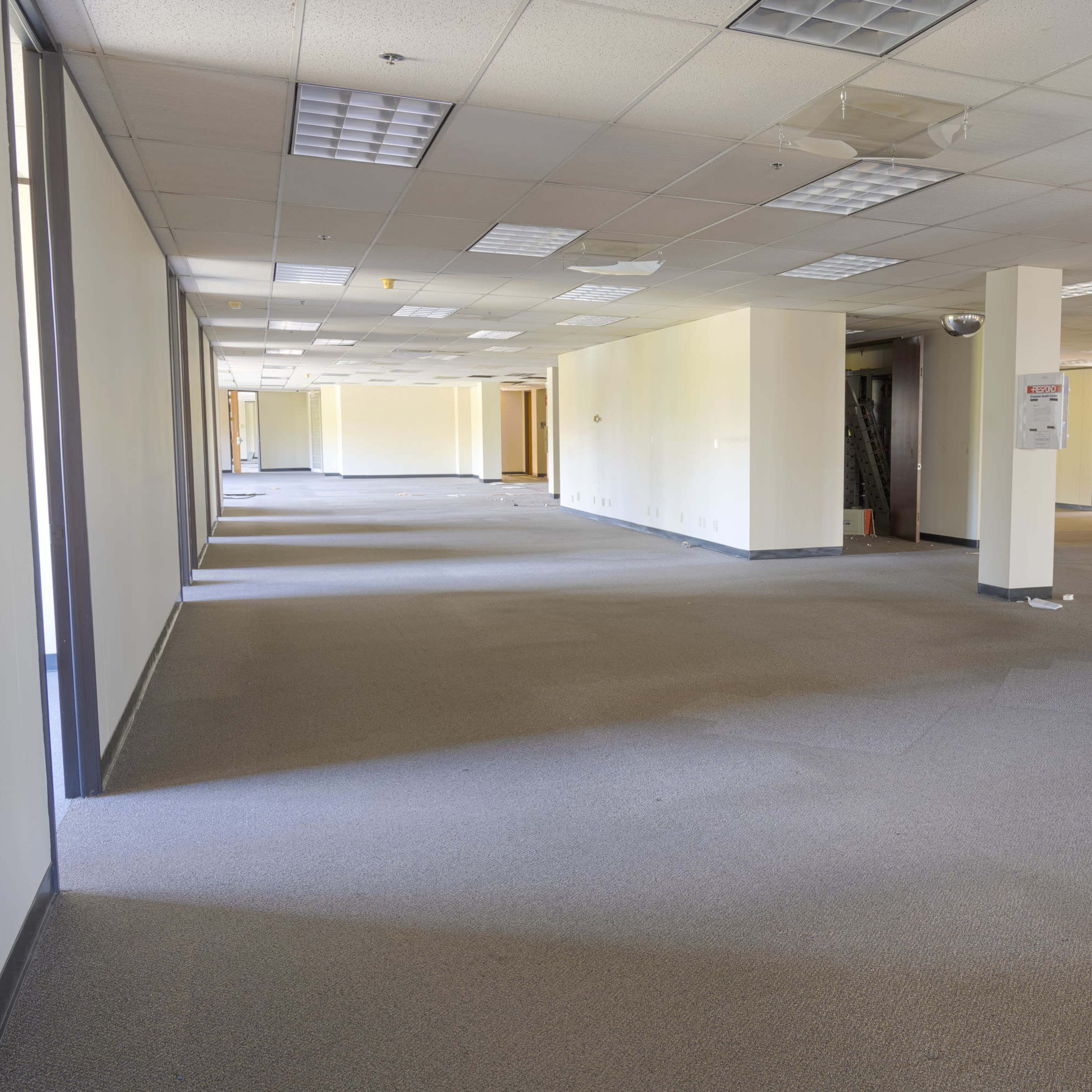 A vacant office space with gray carpet, beige walls, and empty rooms along either side.