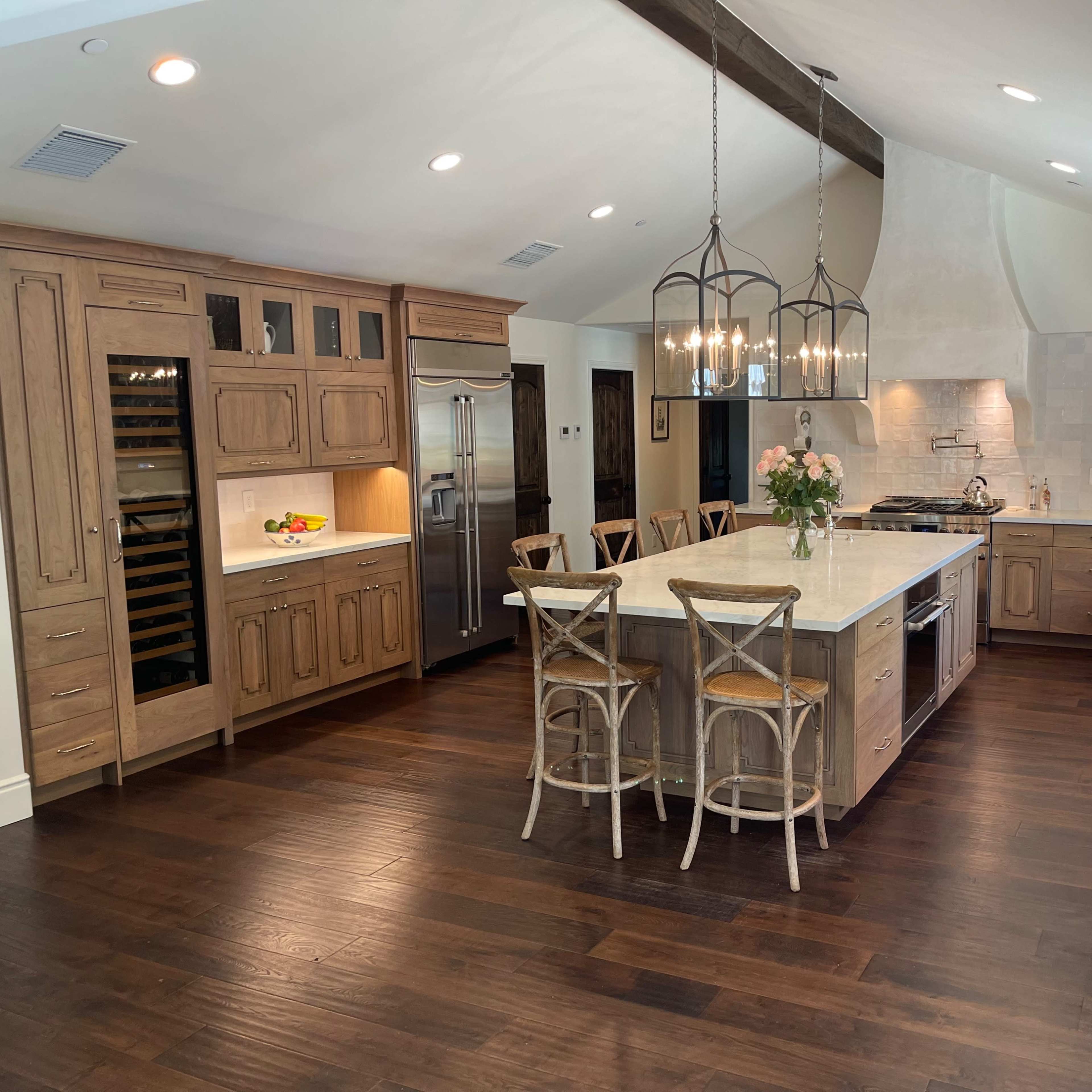 The kitchen features wooden cabinetry, an island with seating, a stainless steel refrigerator, and pendant lighting.