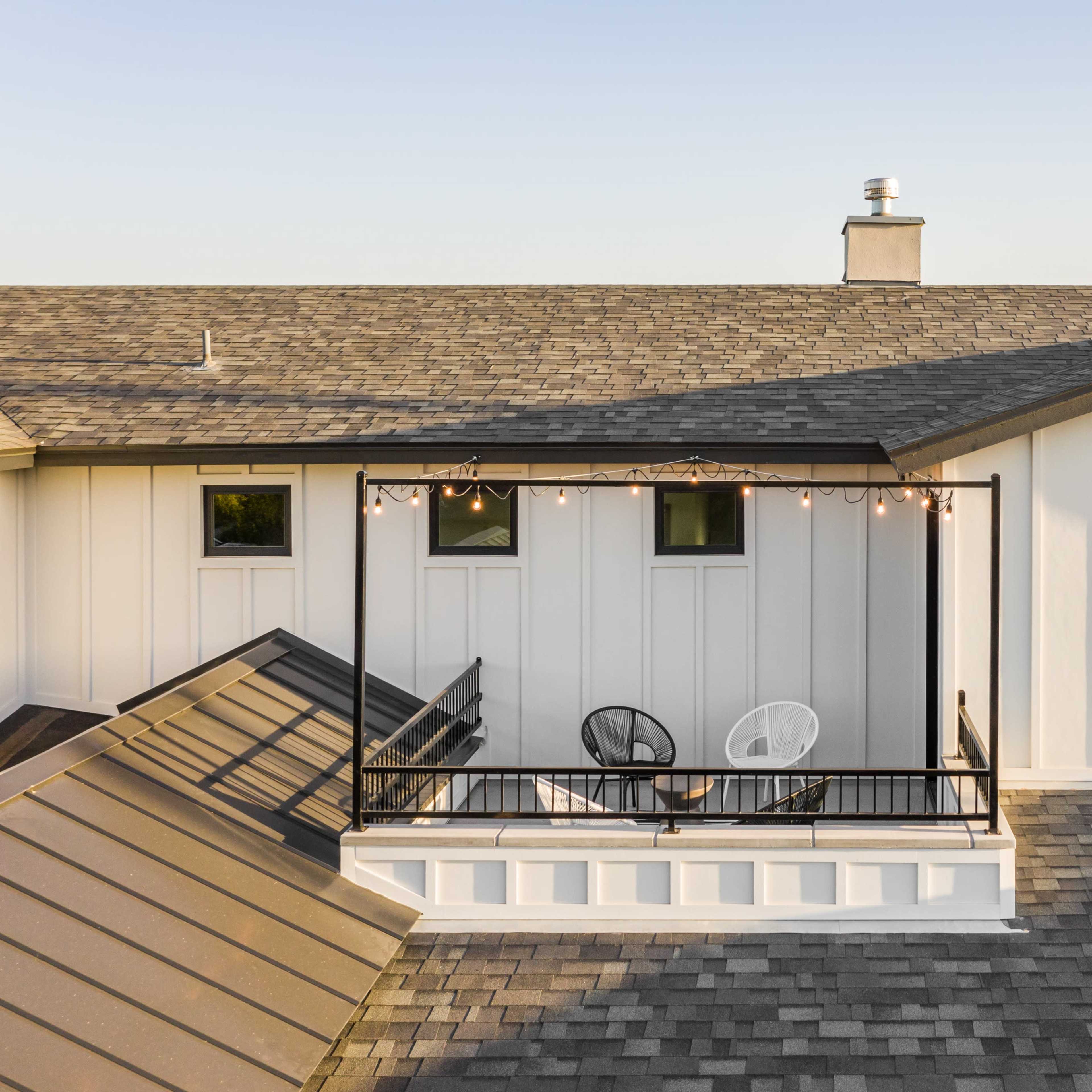 An aerial view of a house with a deck featuring two chairs and string lights, surrounded by sloped roofs.