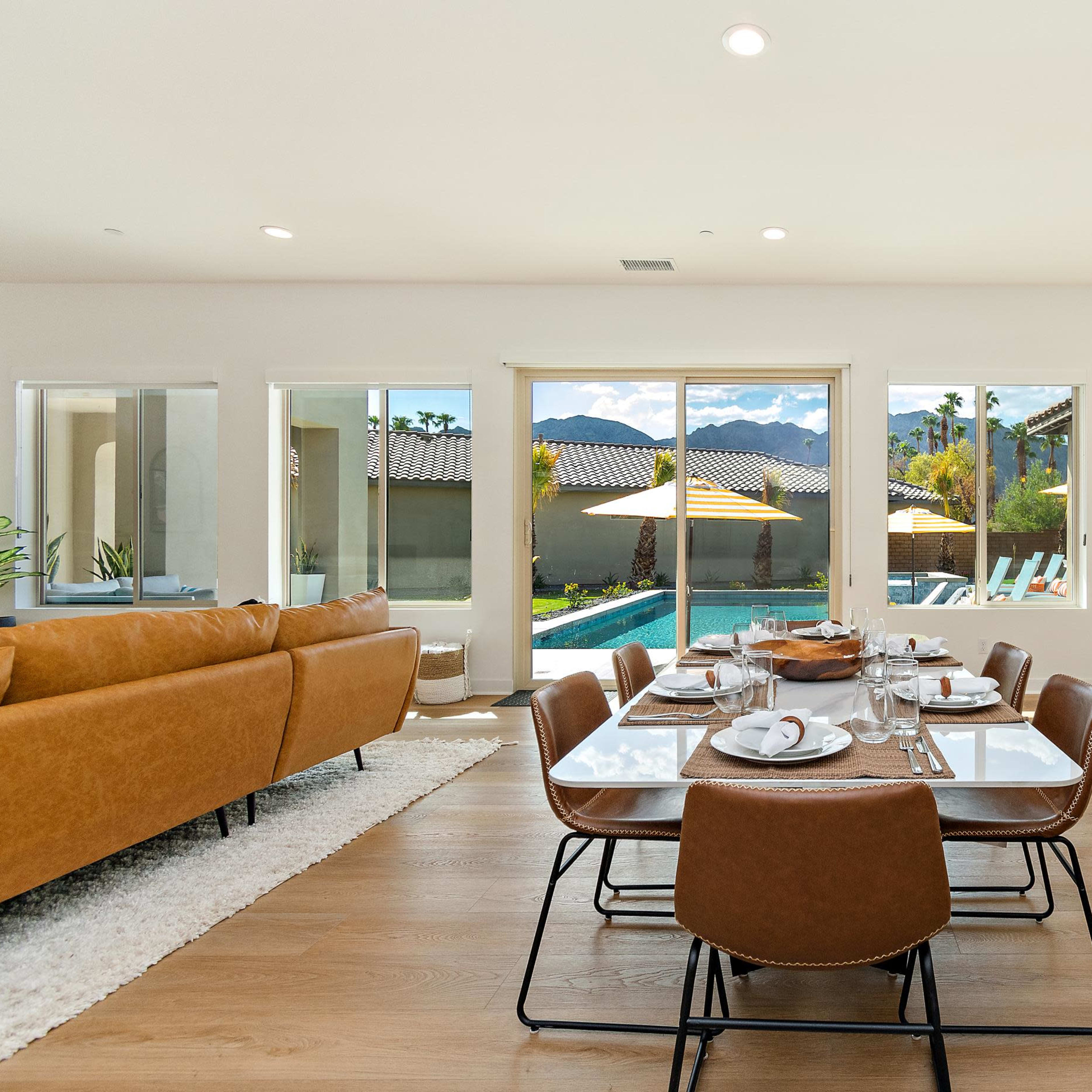 A modern dining area with a large table set for a meal, overlooking a pool and outdoor space through large windows.