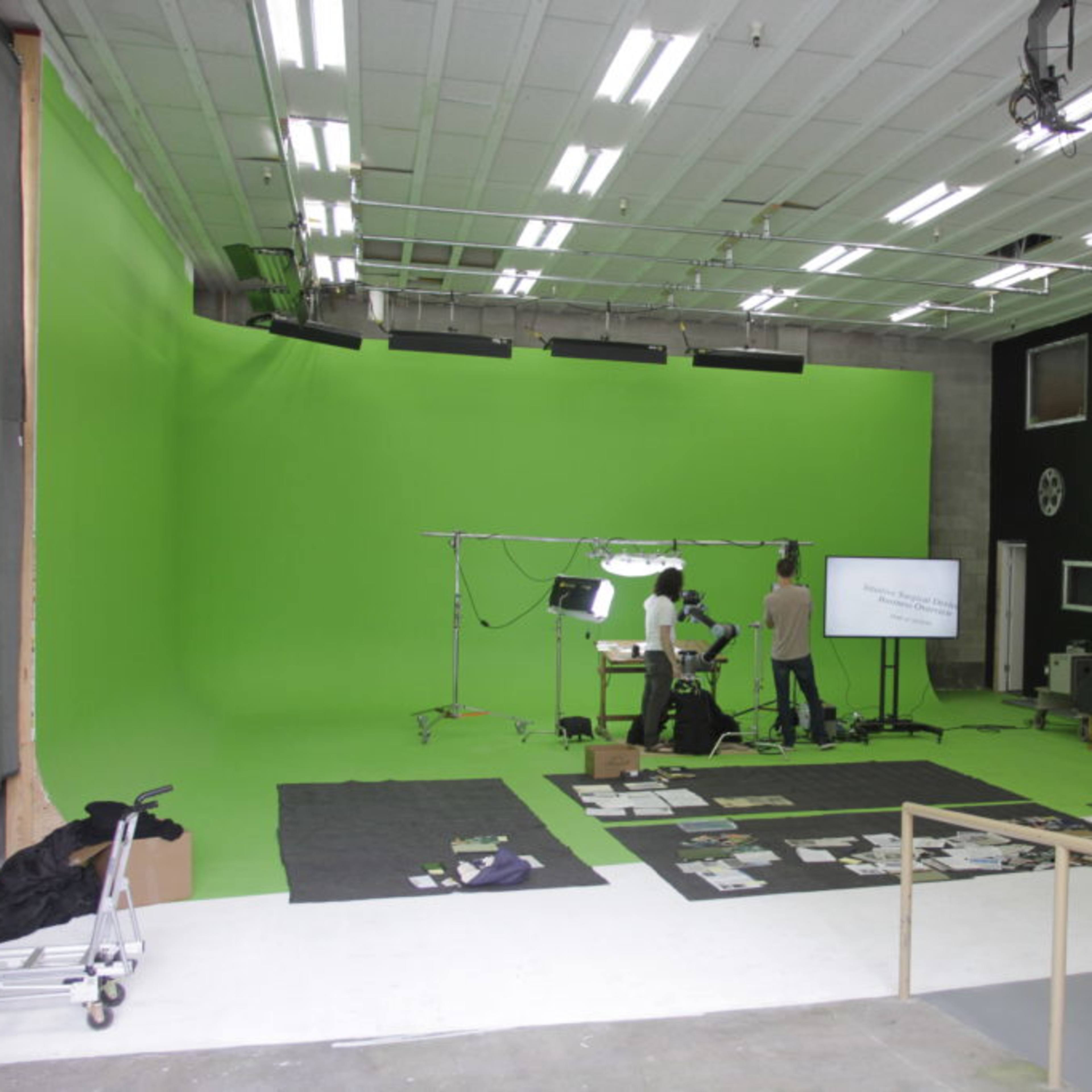 A green screen studio setup with lighting equipment, a camera, and a monitor in a spacious room.