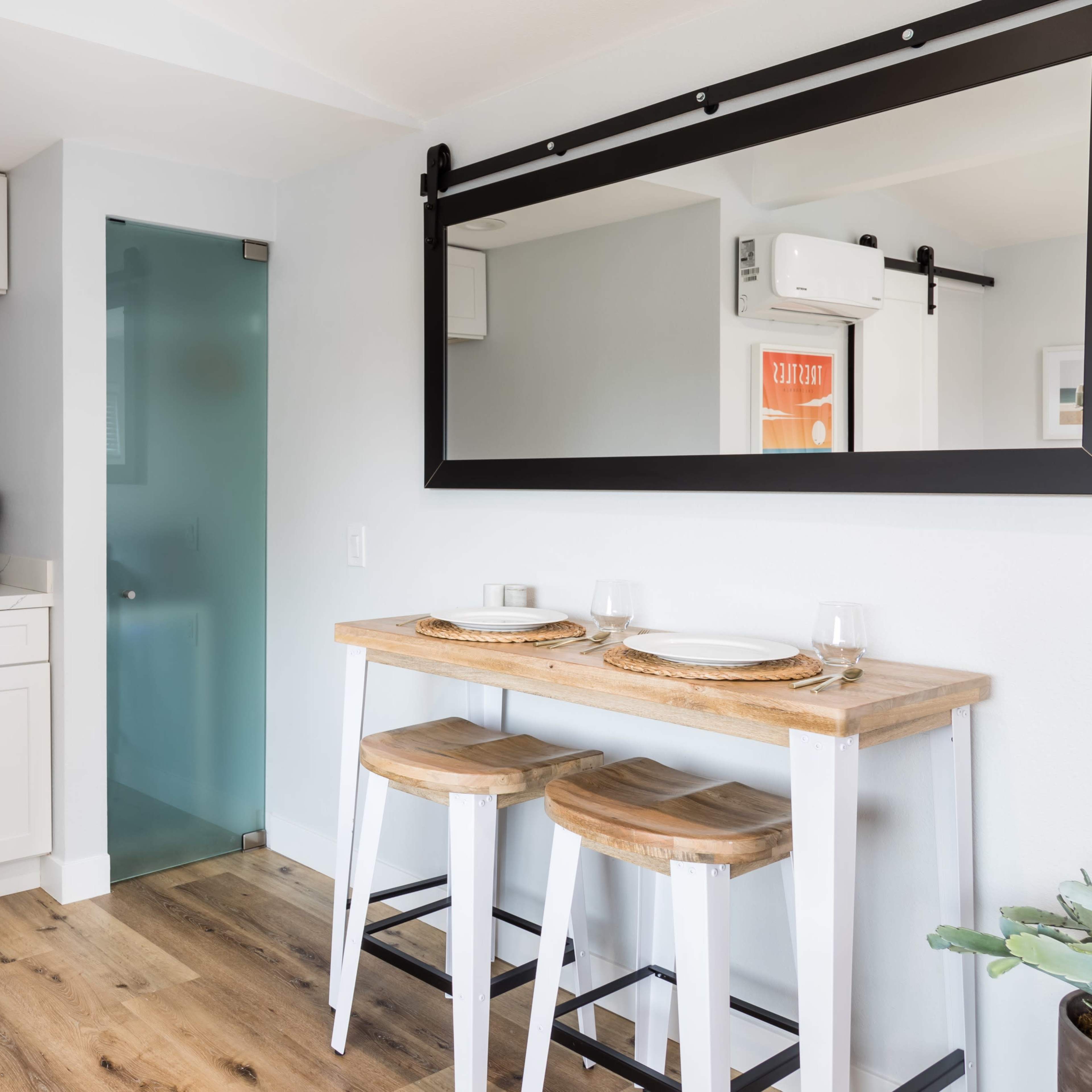 A small kitchen area features a bar table with two stools, a kitchenette, and a mirror above the table.