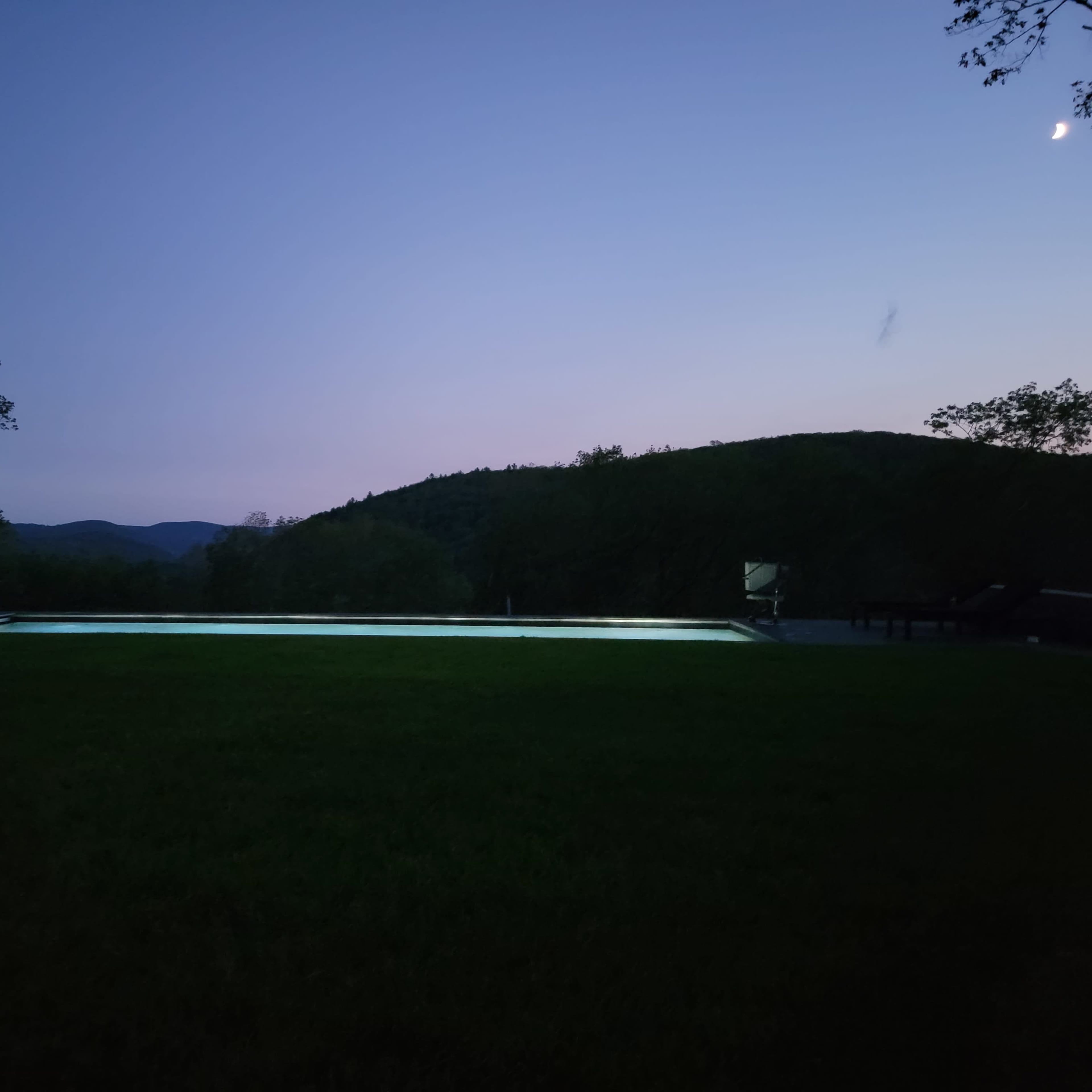 A lit swimming pool set against a twilight sky and rolling hills.