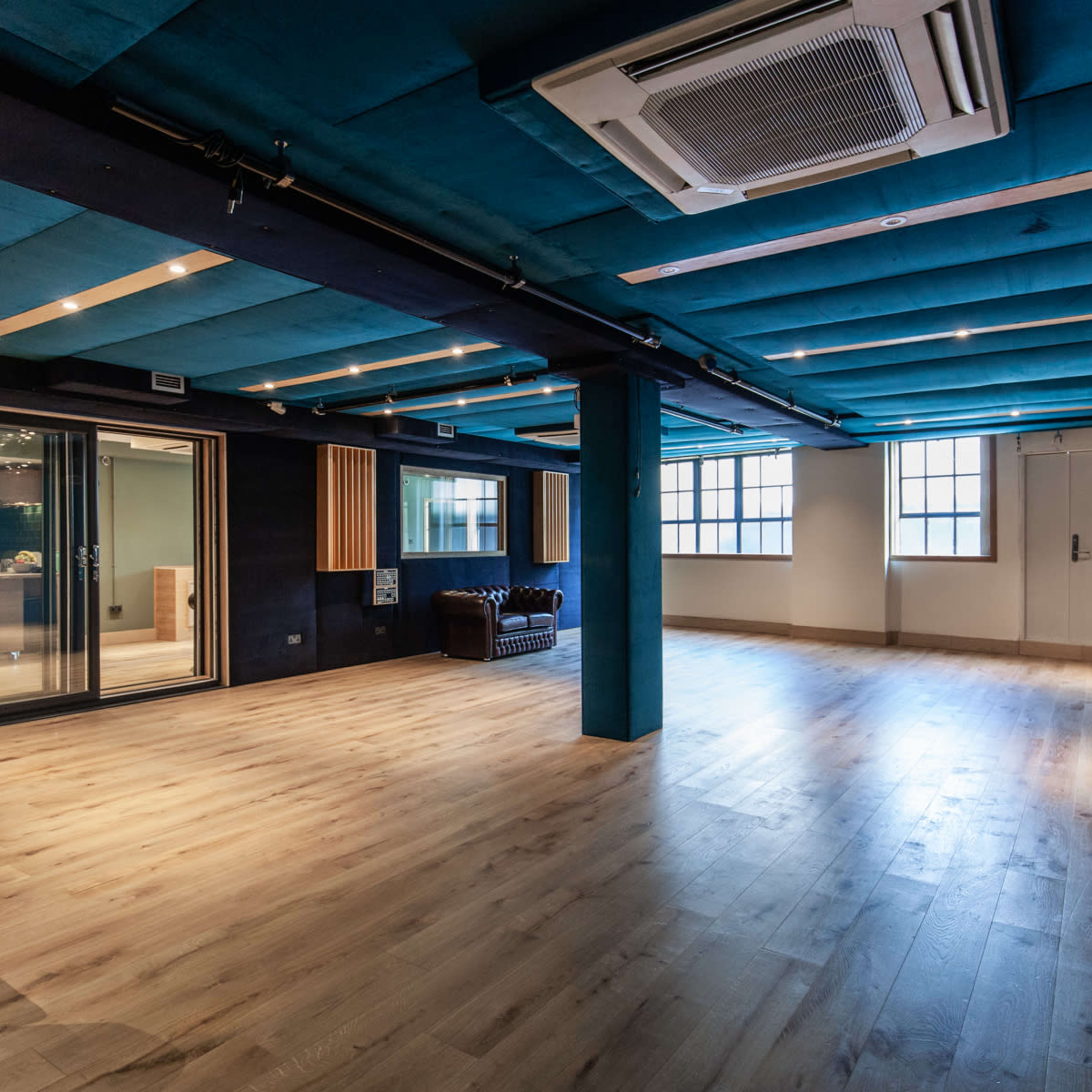 A spacious room with blue acoustic panels, wooden flooring, and large glass doors leading to another area.
