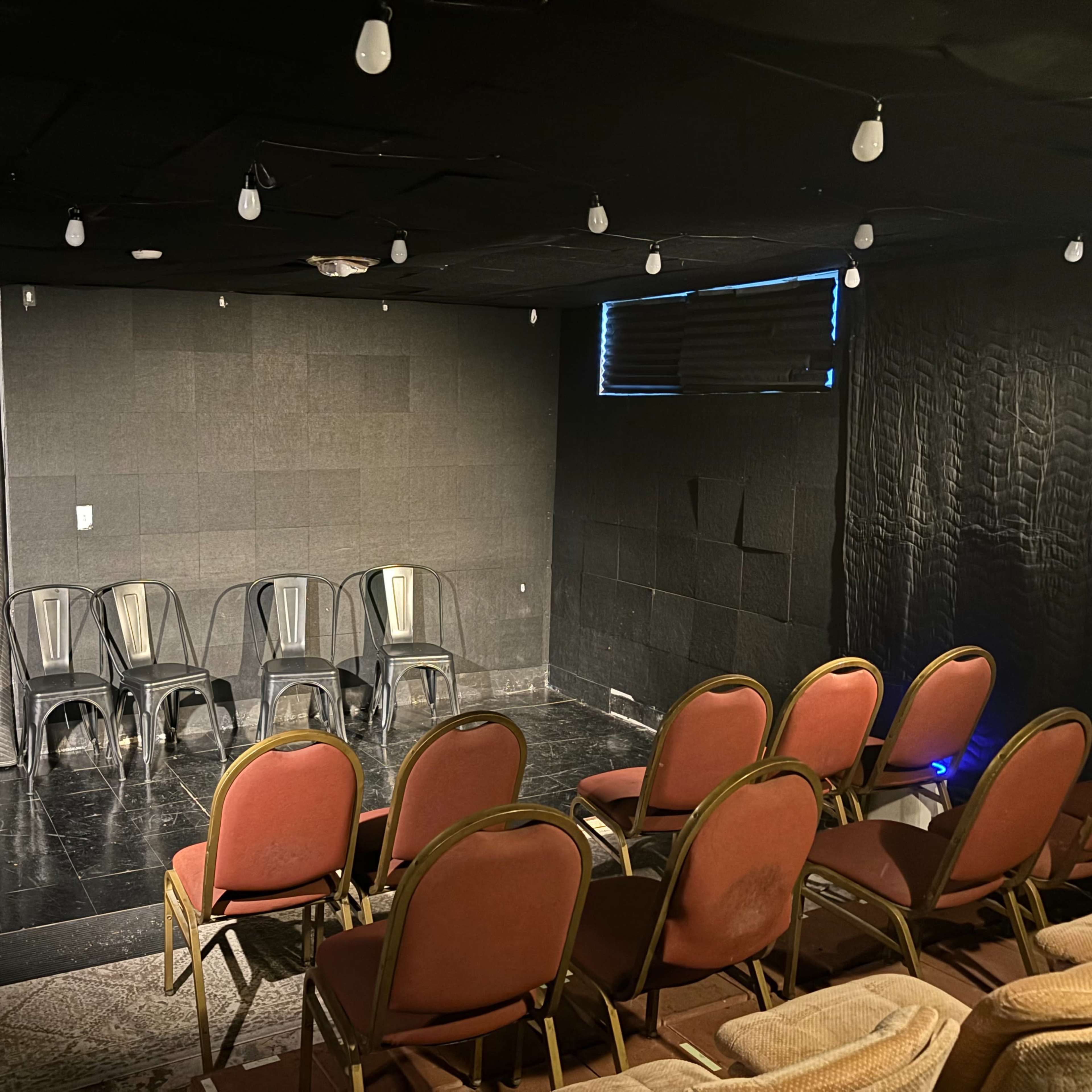 A small theater with black walls, a stage area, and rows of red chairs arranged for an audience.
