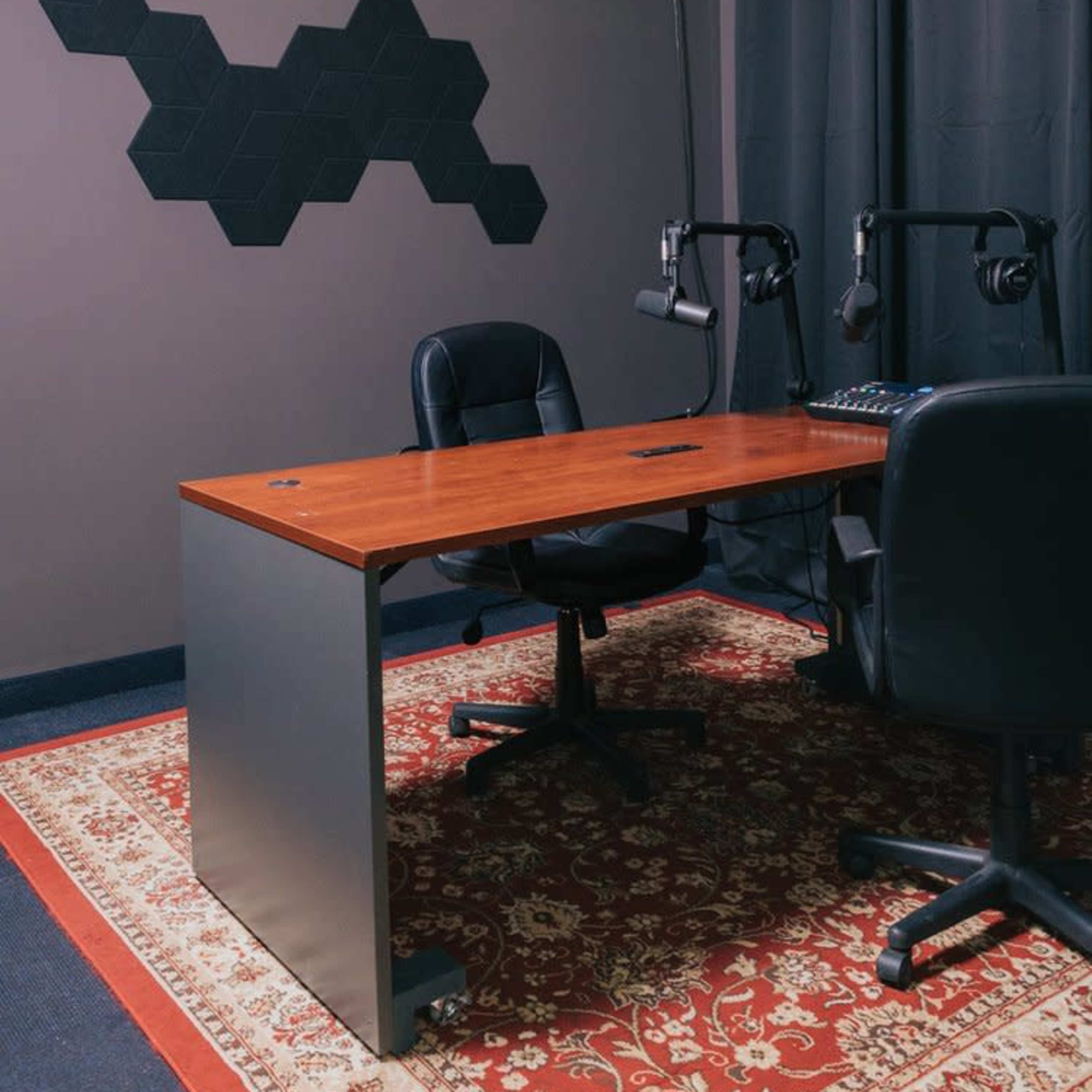 A small recording studio with a wooden table, two chairs, and a backdrop of colorful foam panels and hexagonal wall decor.