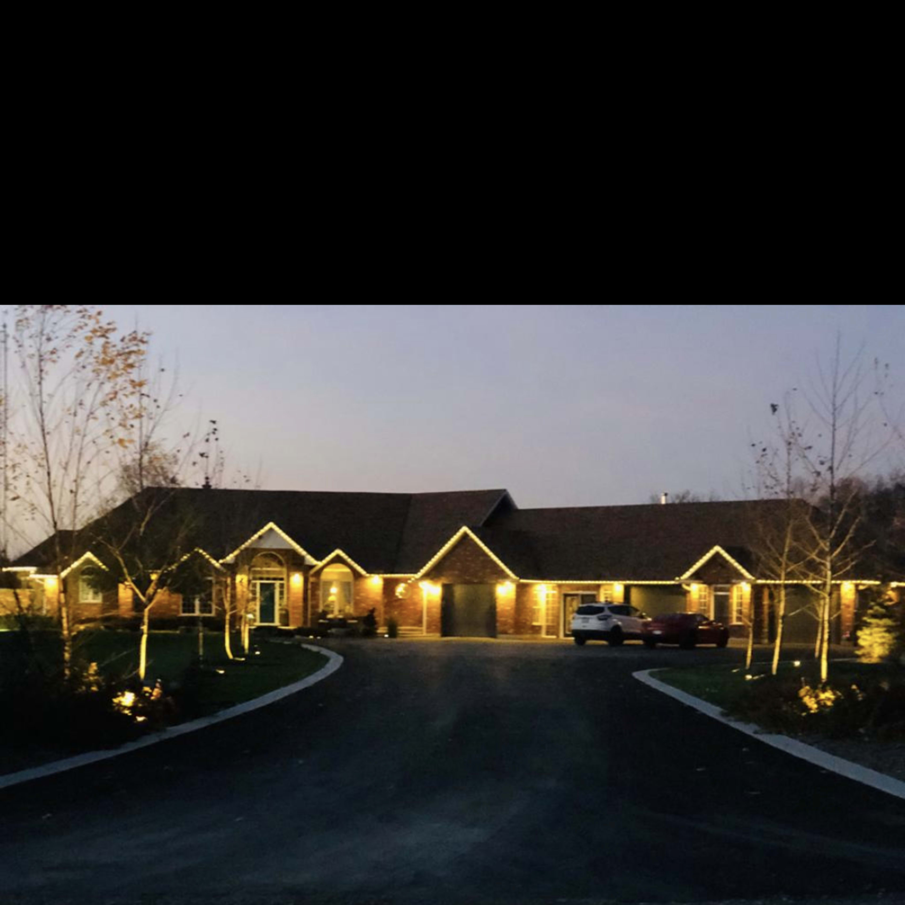 A well-lit residential building with a circular driveway, surrounded by trees at dusk.