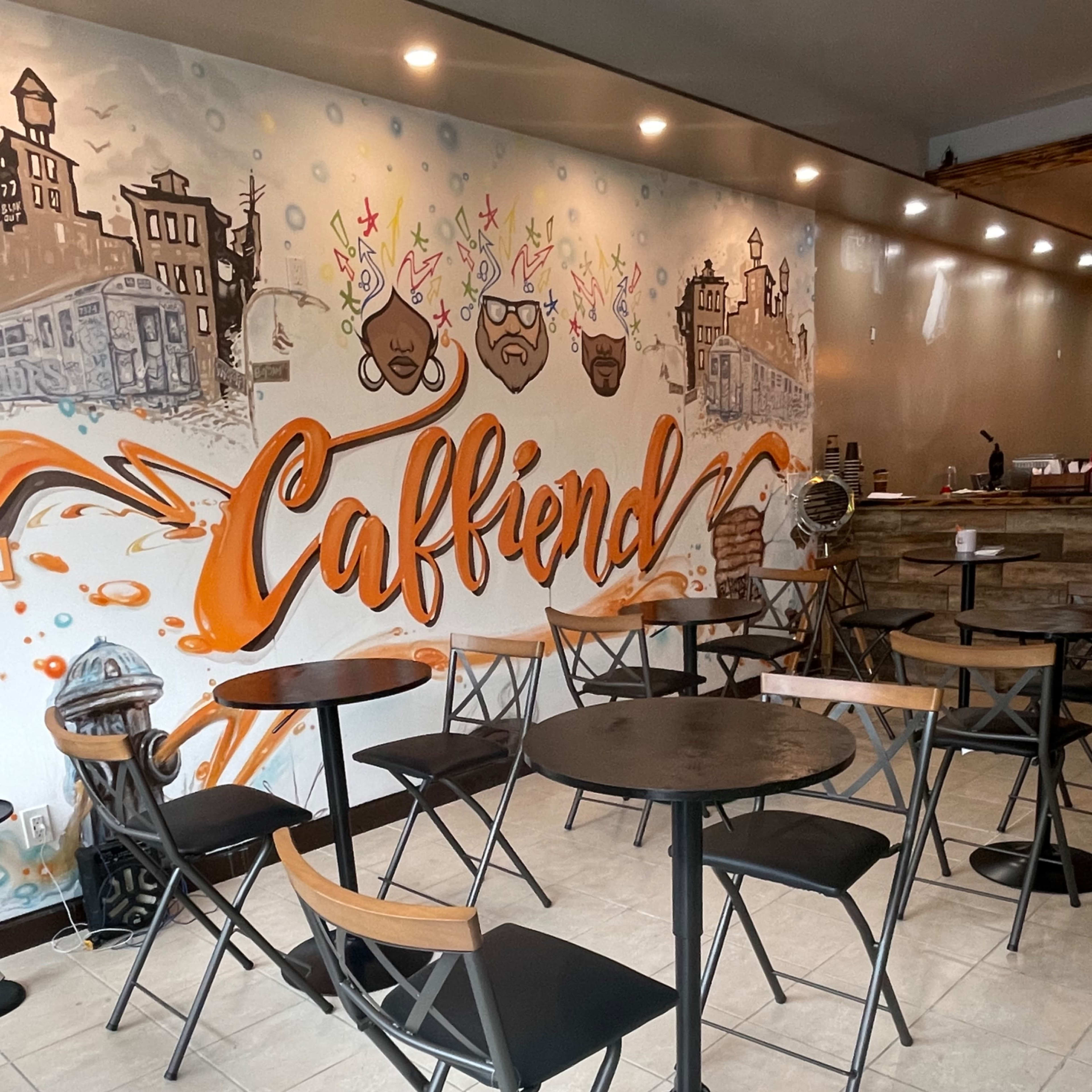 A coffee shop interior with a mural featuring the word "Caffiend" and several empty tables and chairs arranged in the space.