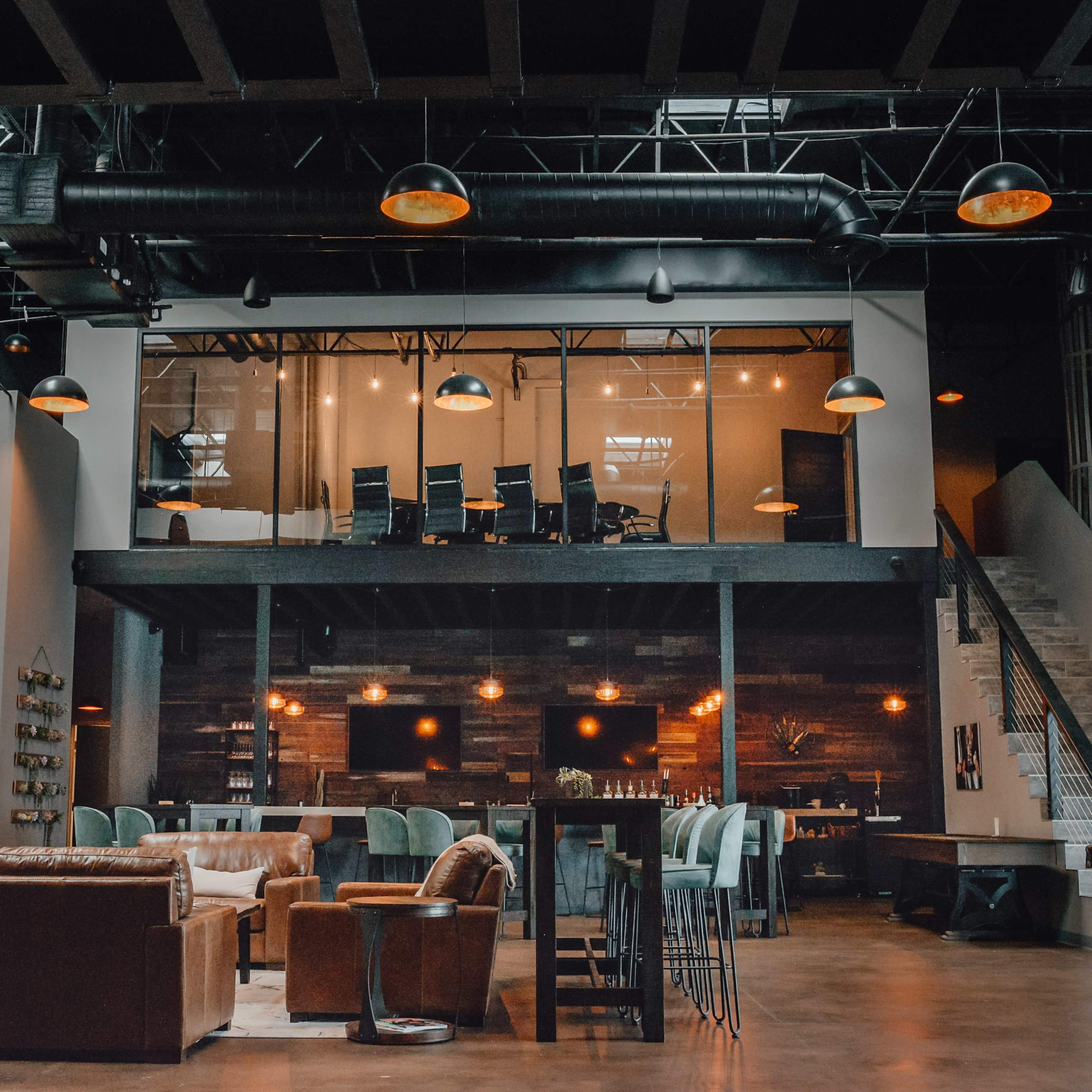 A modern, open-concept lounge area with a seating arrangement on the lower level and a glass-enclosed meeting space above.