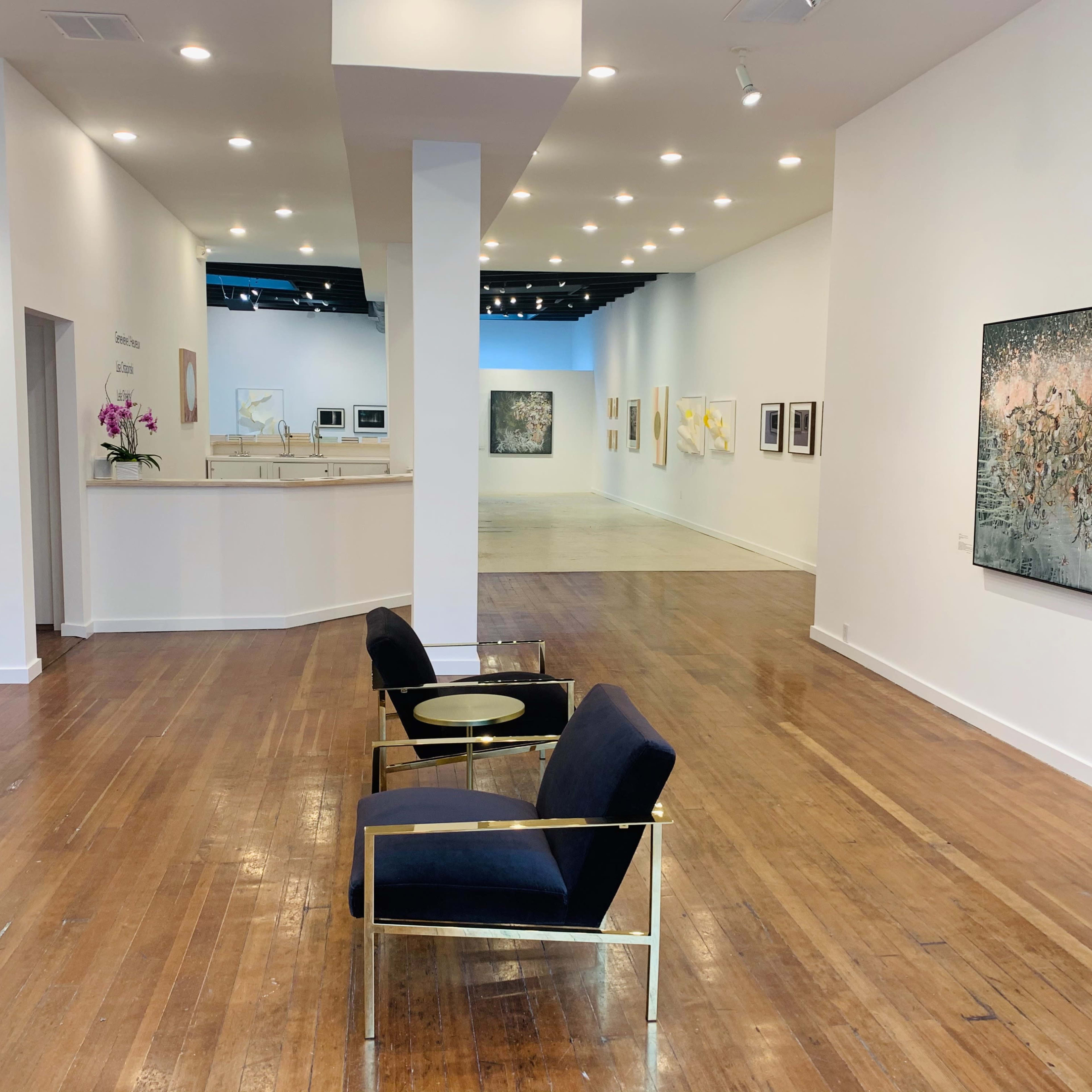 A modern gallery space with a reception area,white walls adorned with framed artwork, and a seating area featuring contemporary chairs.
