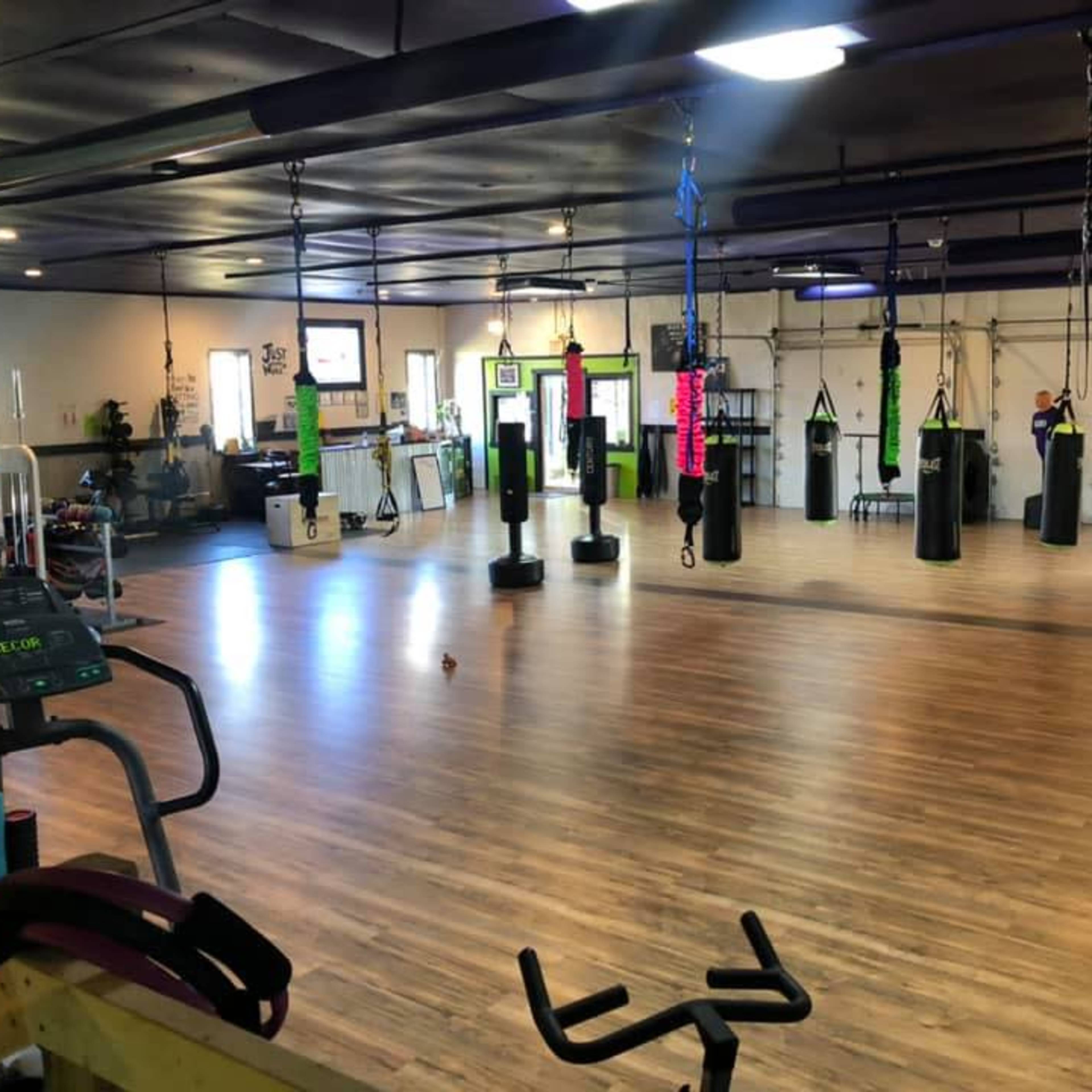 A spacious gym with various punching bags hanging from the ceiling and exercise equipment positioned around the wooden floor.