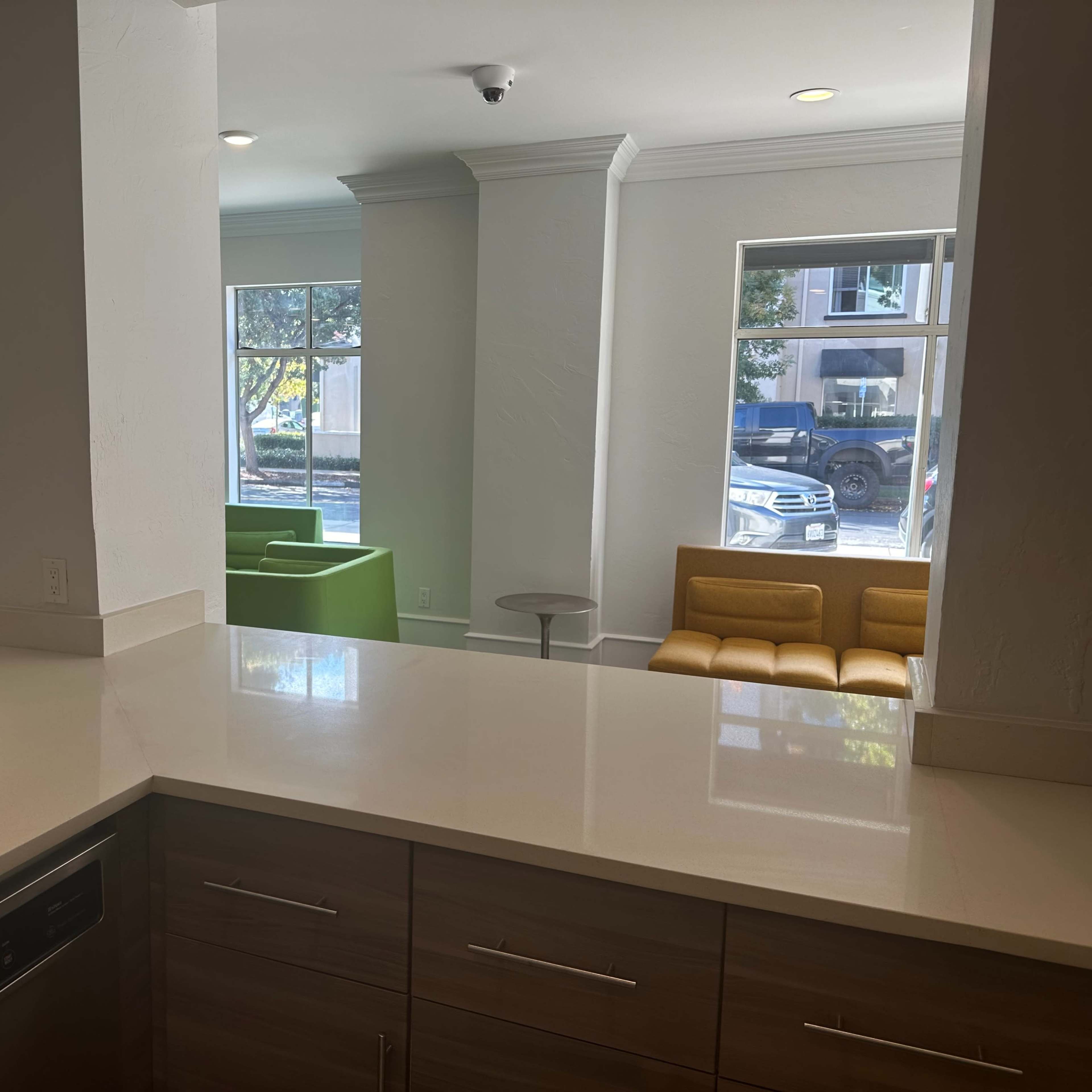 A modern interior space with a kitchen view, featuring a countertop, stainless steel appliances, and a lounge area with green and orange seating.