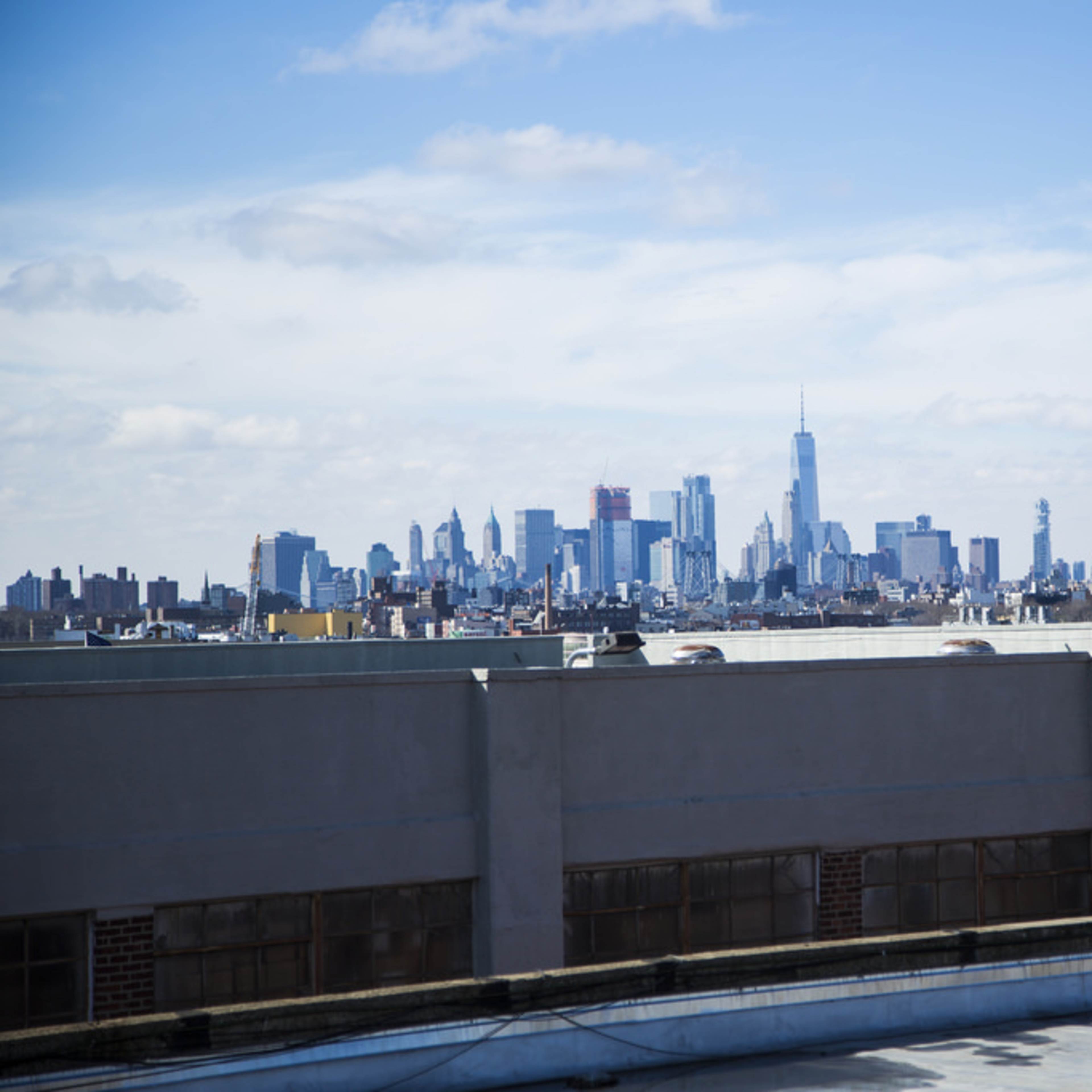 A skyline view of a city, featuring tall buildings and a prominent skyscraper under a blue sky with scattered clouds.