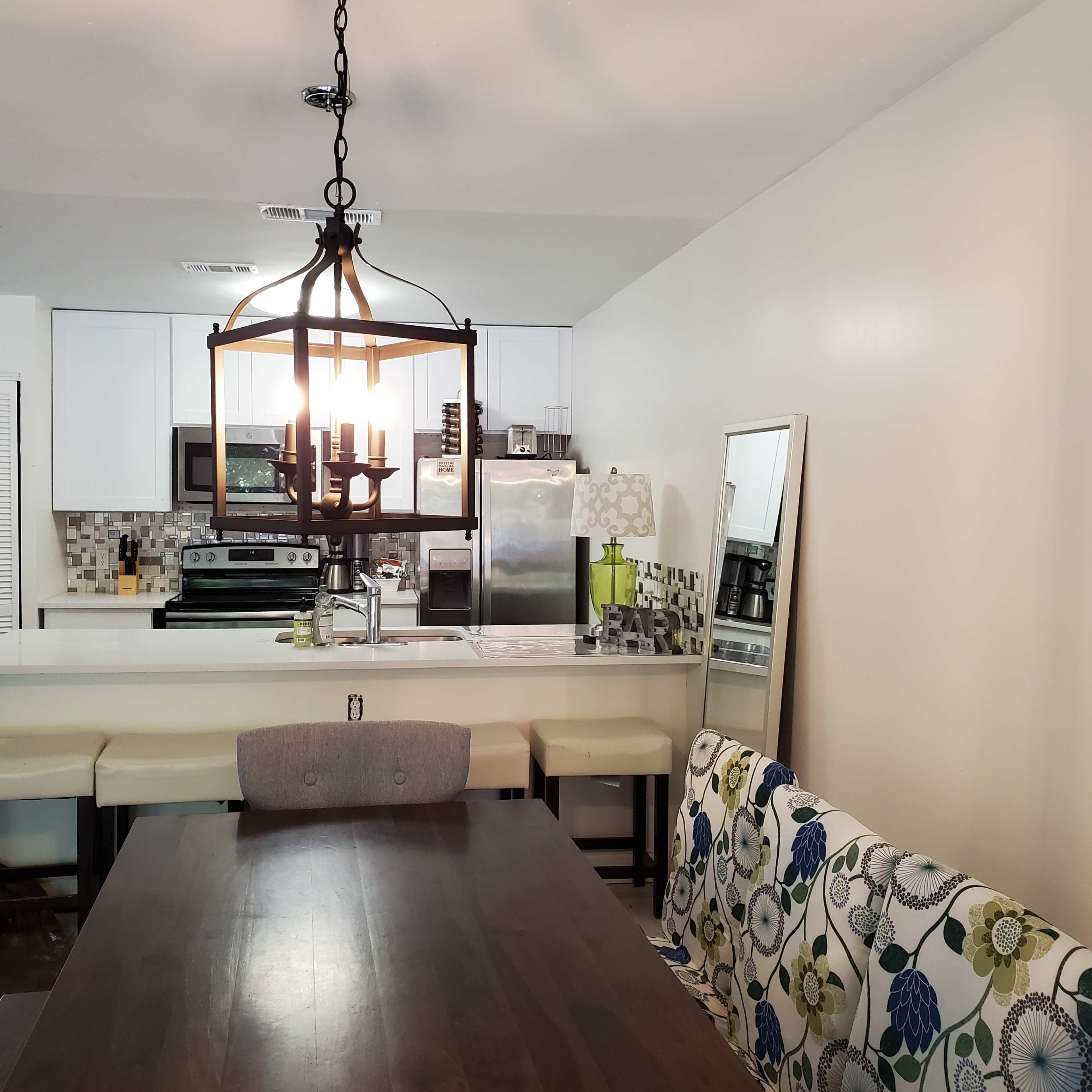 A dining area with a wooden table, a patterned sofa, and an attached kitchen featuring white cabinets and stainless steel appliances.