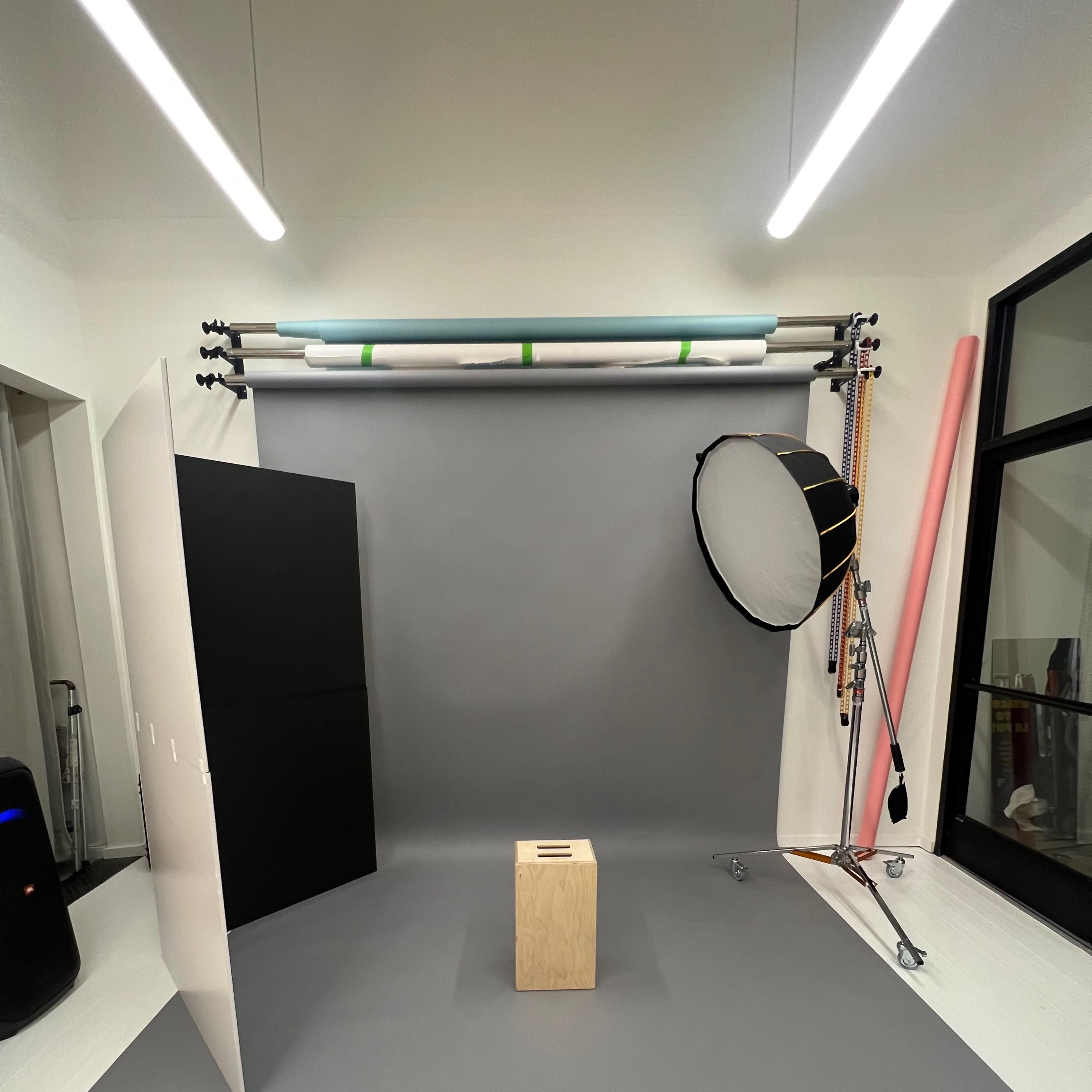 A photo studio setup with a gray background, a wooden block in the center, and lighting equipment arranged around the space.