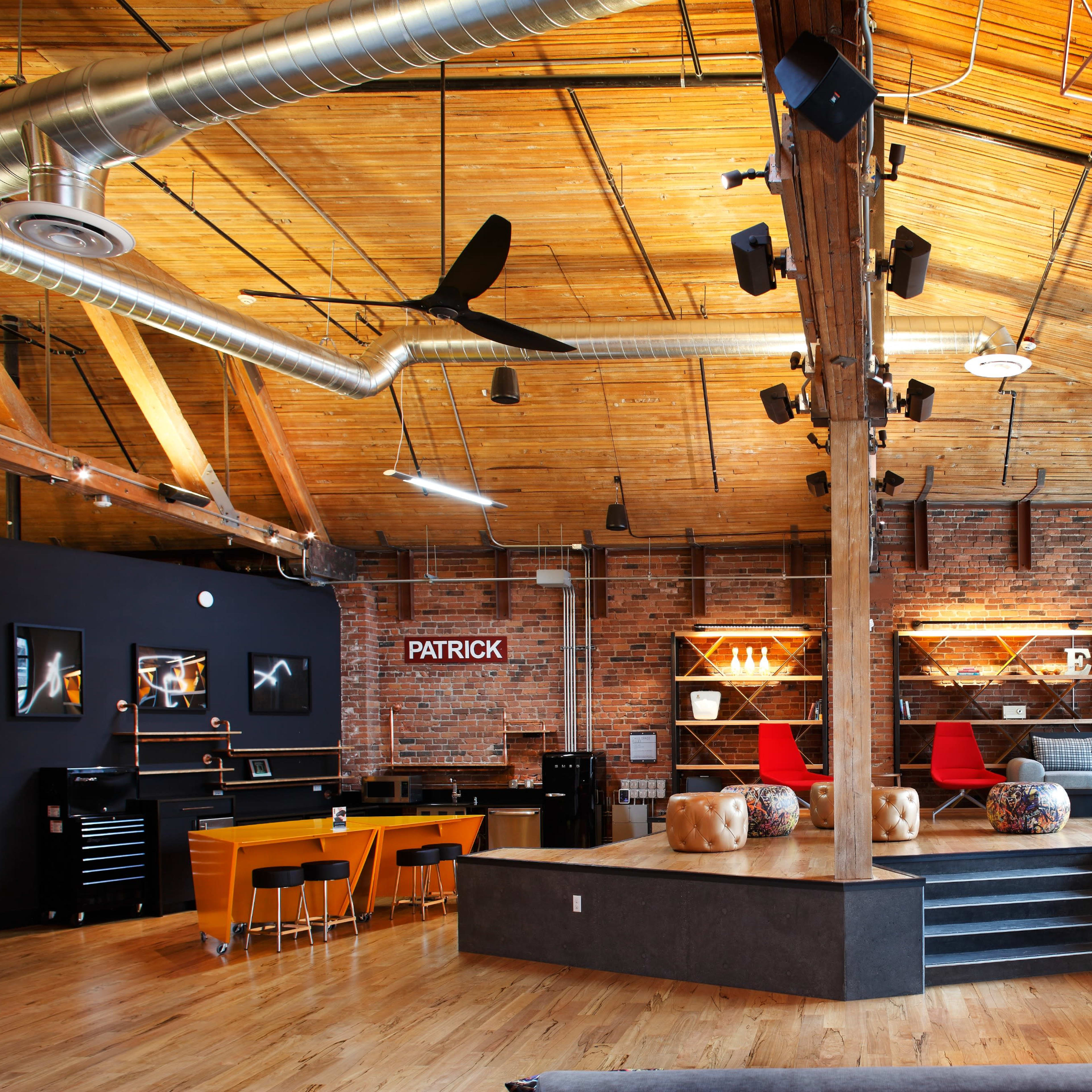 A spacious loft-style interior with a high wooden ceiling, exposed brick walls, and a seating area featuring modern furniture and decorative shelves.