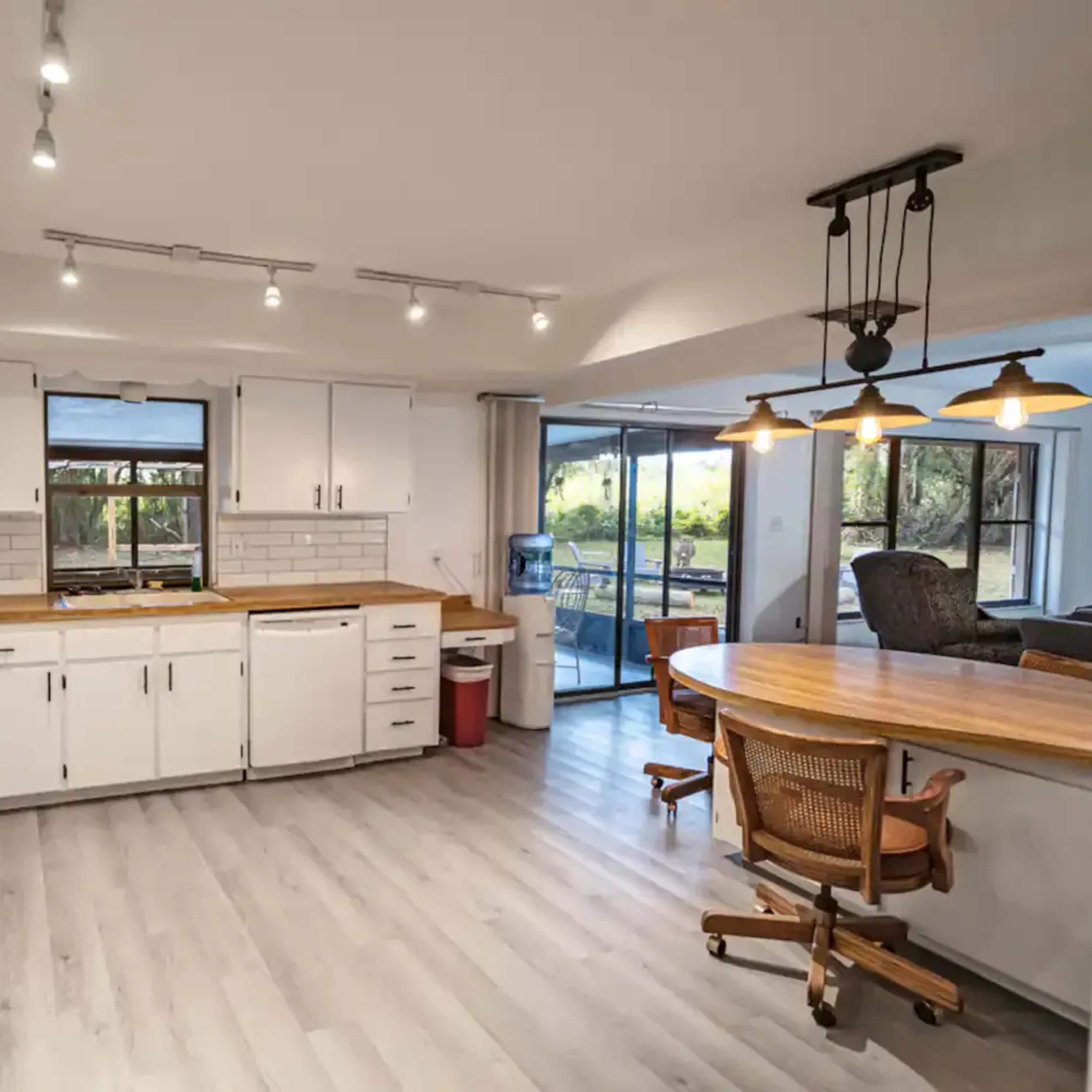A clean kitchen features white cabinets, a wooden countertop, and large windows that provide natural light.