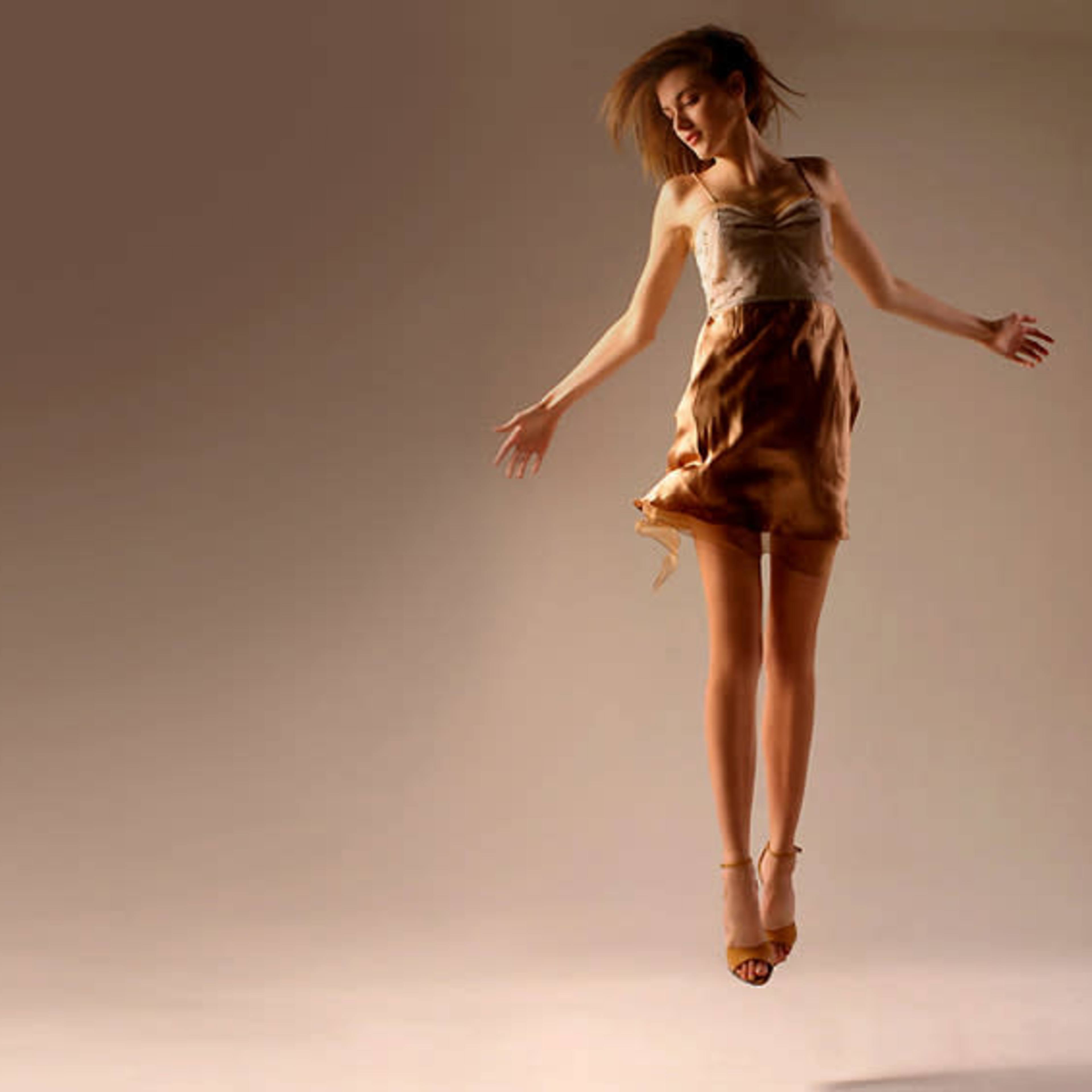 A woman in a dress appears to be suspended in mid-air against a neutral background.