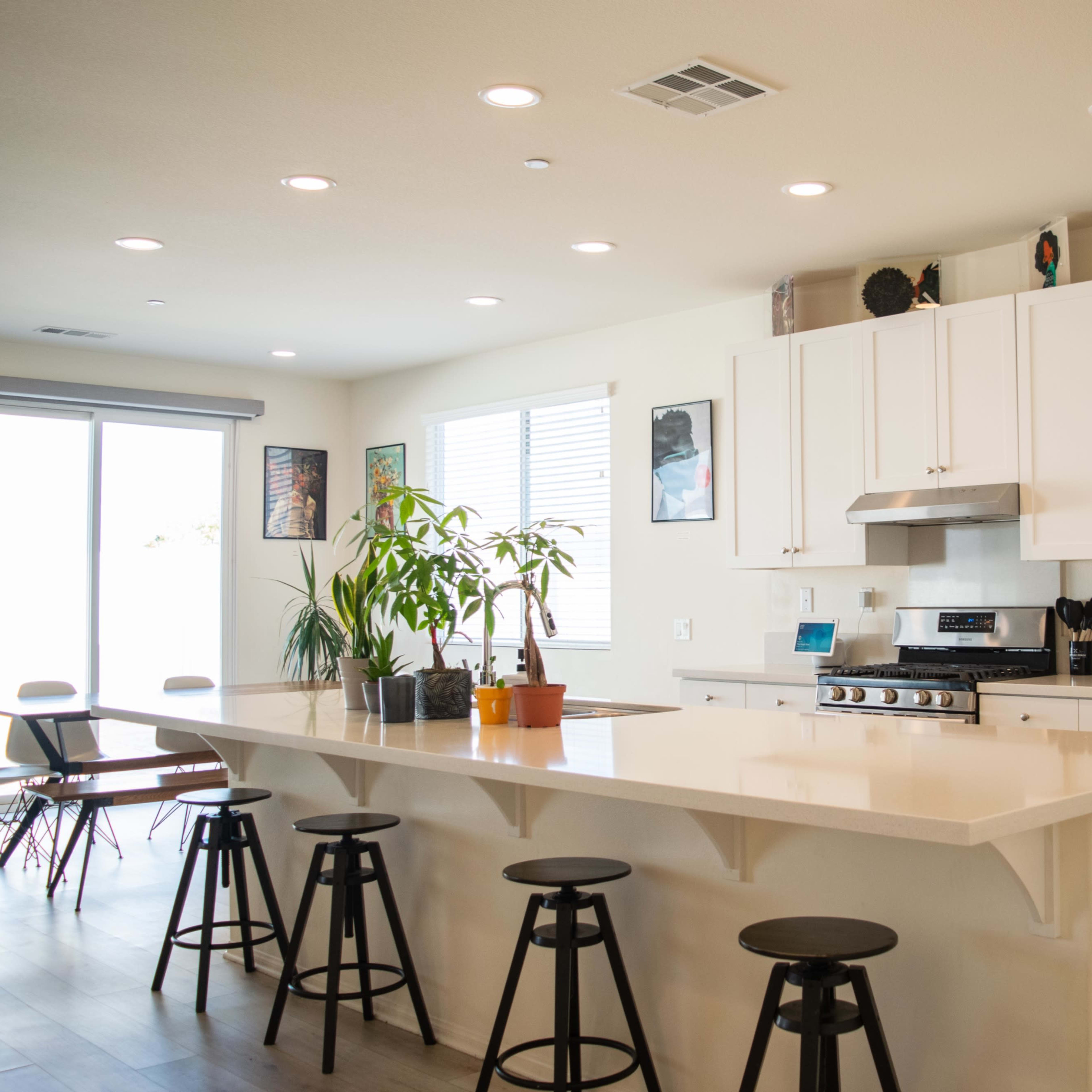 A modern kitchen features a central island with stools, white cabinetry, and stainless steel appliances.