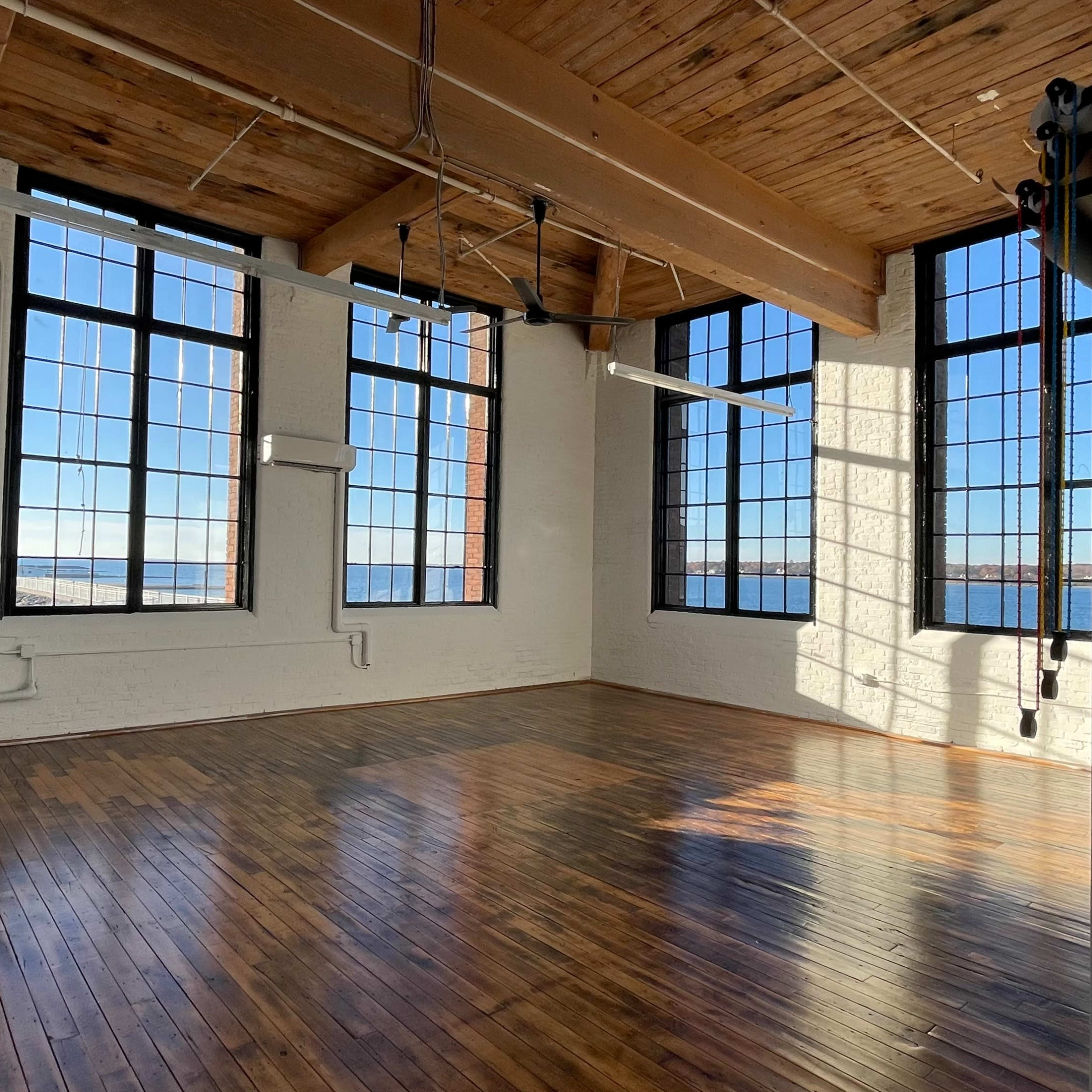 A spacious, well-lit room with large windows and polished wooden floors.