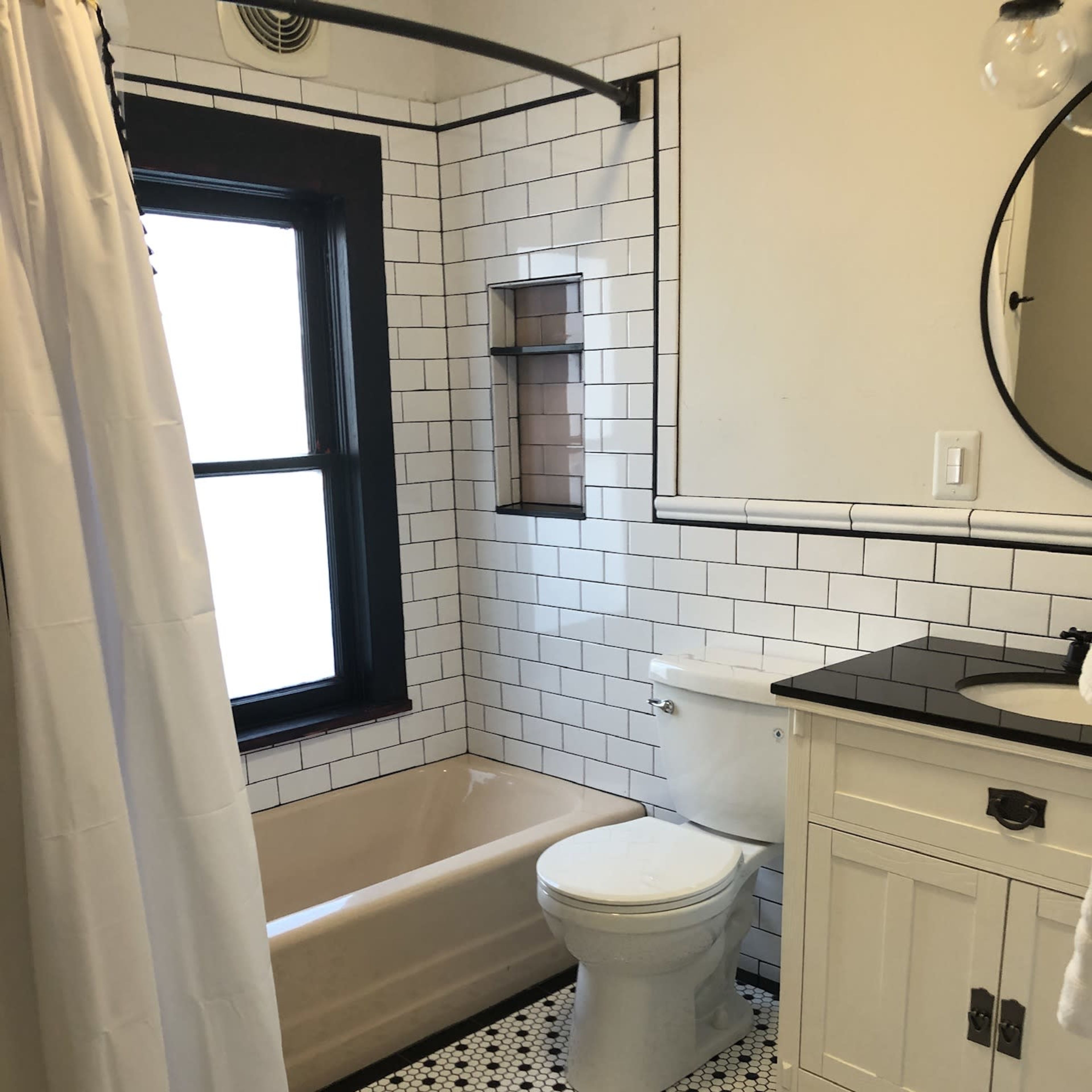 A bathroom featuring a bathtub, toilet, sink with a cabinet, white shower curtain, and black and white tiled floor.