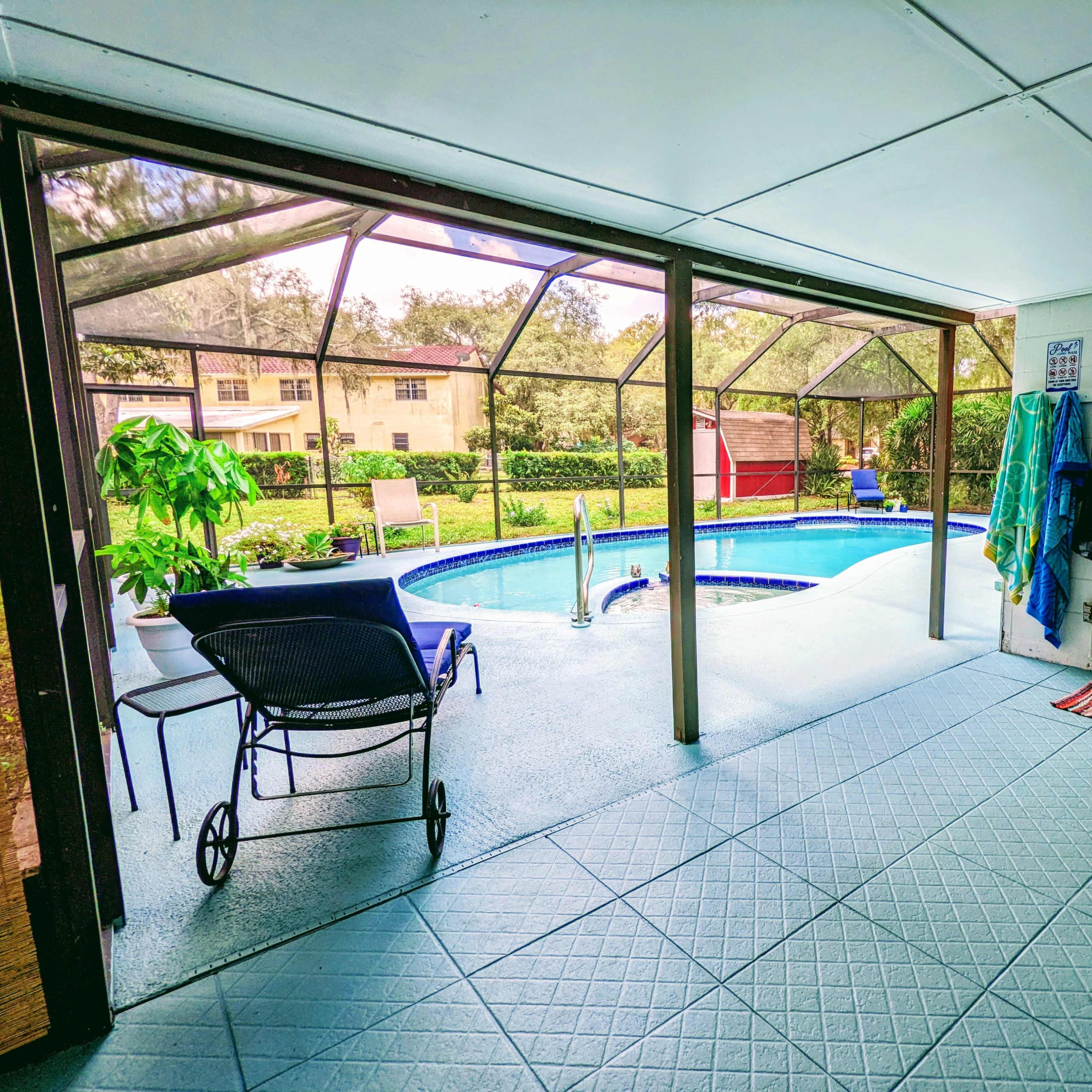 A screened patio overlooking a pool area, with a chair and plants visible, and a view of the surrounding landscaping.