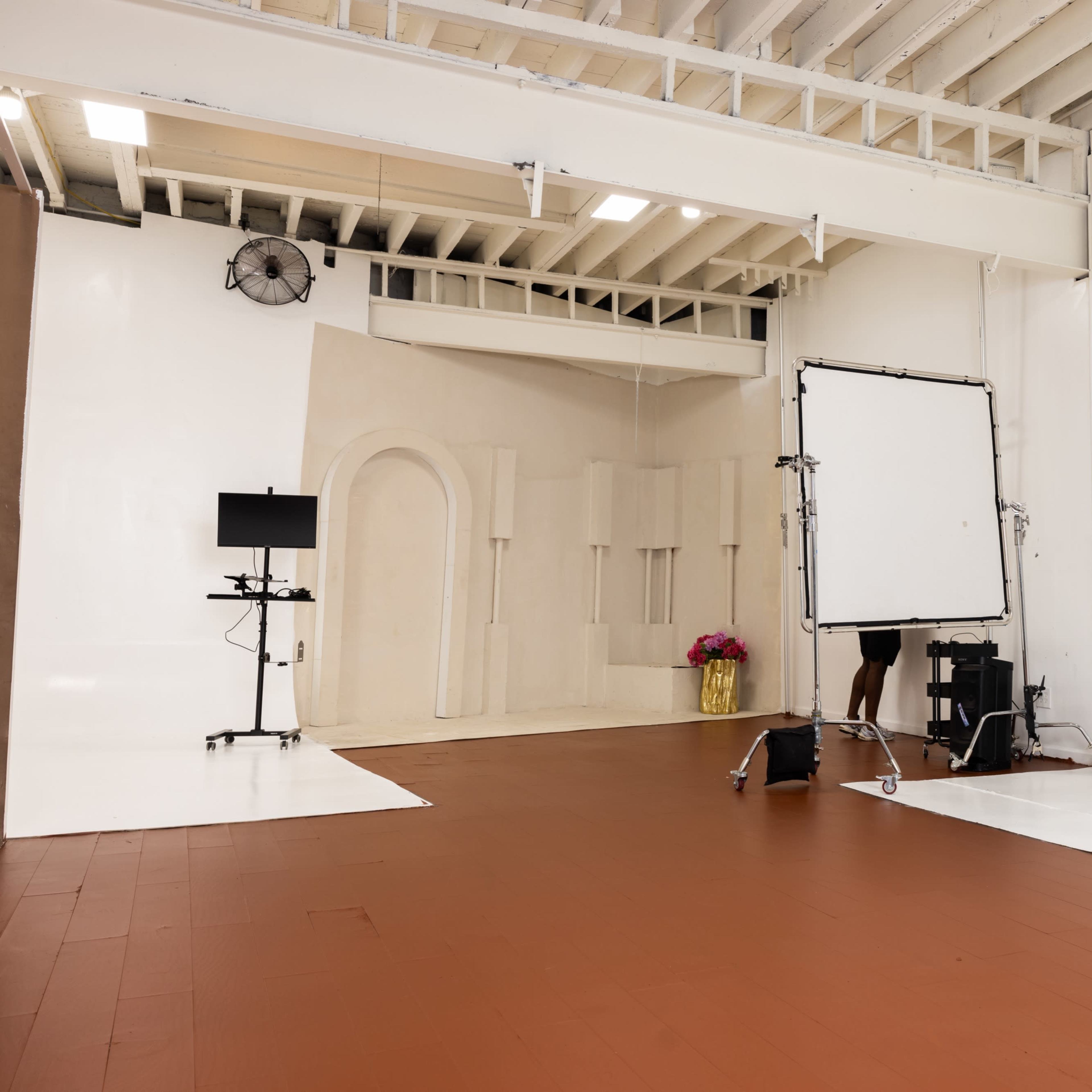 A spacious photography studio with a wooden floor, white walls, and various equipment arranged for a photoshoot.