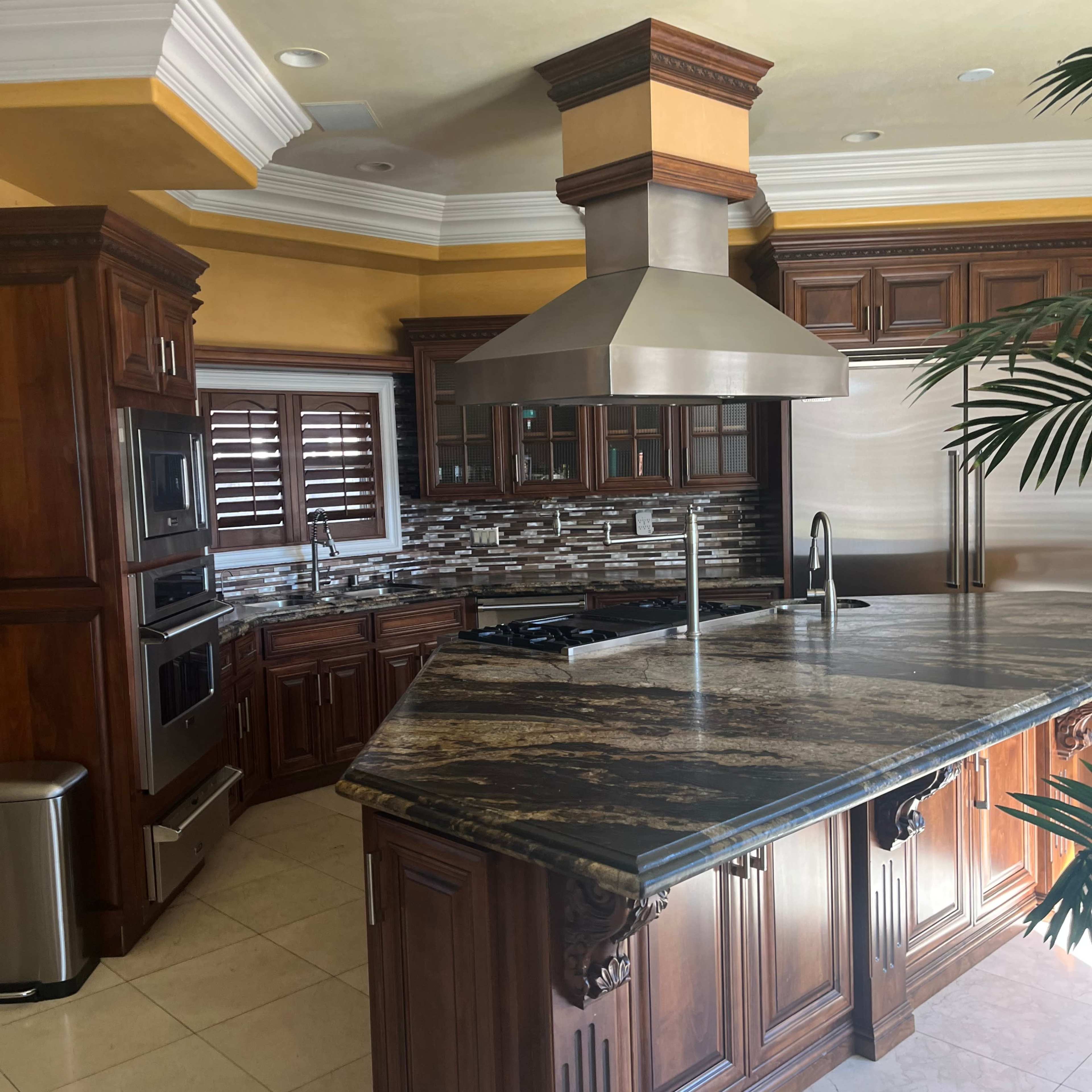 A spacious kitchen features dark wood cabinetry, a large granite countertop island, and stainless steel appliances.