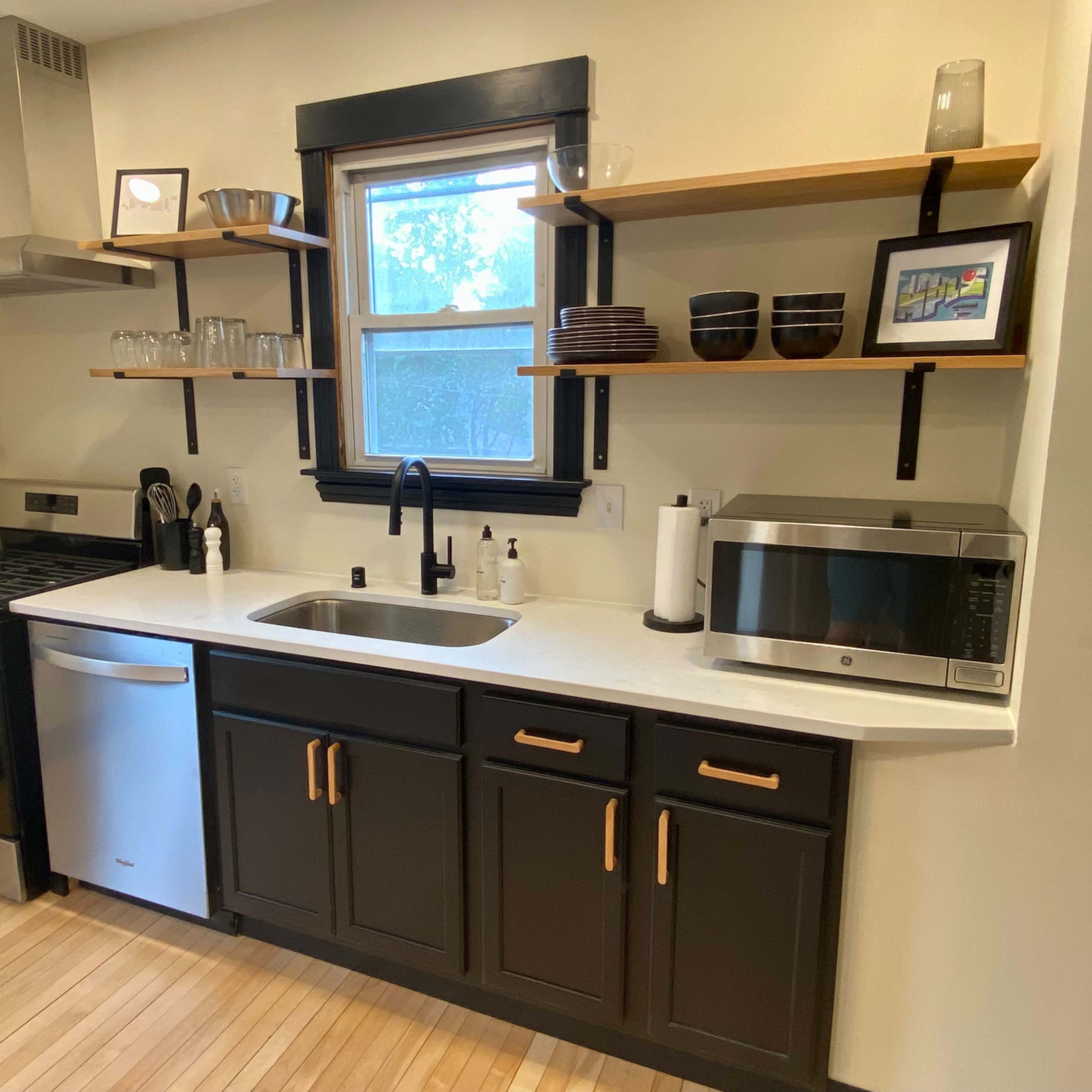 A modern kitchen features a stainless steel stove, a microwave, and open shelving with various dishes and glassware.