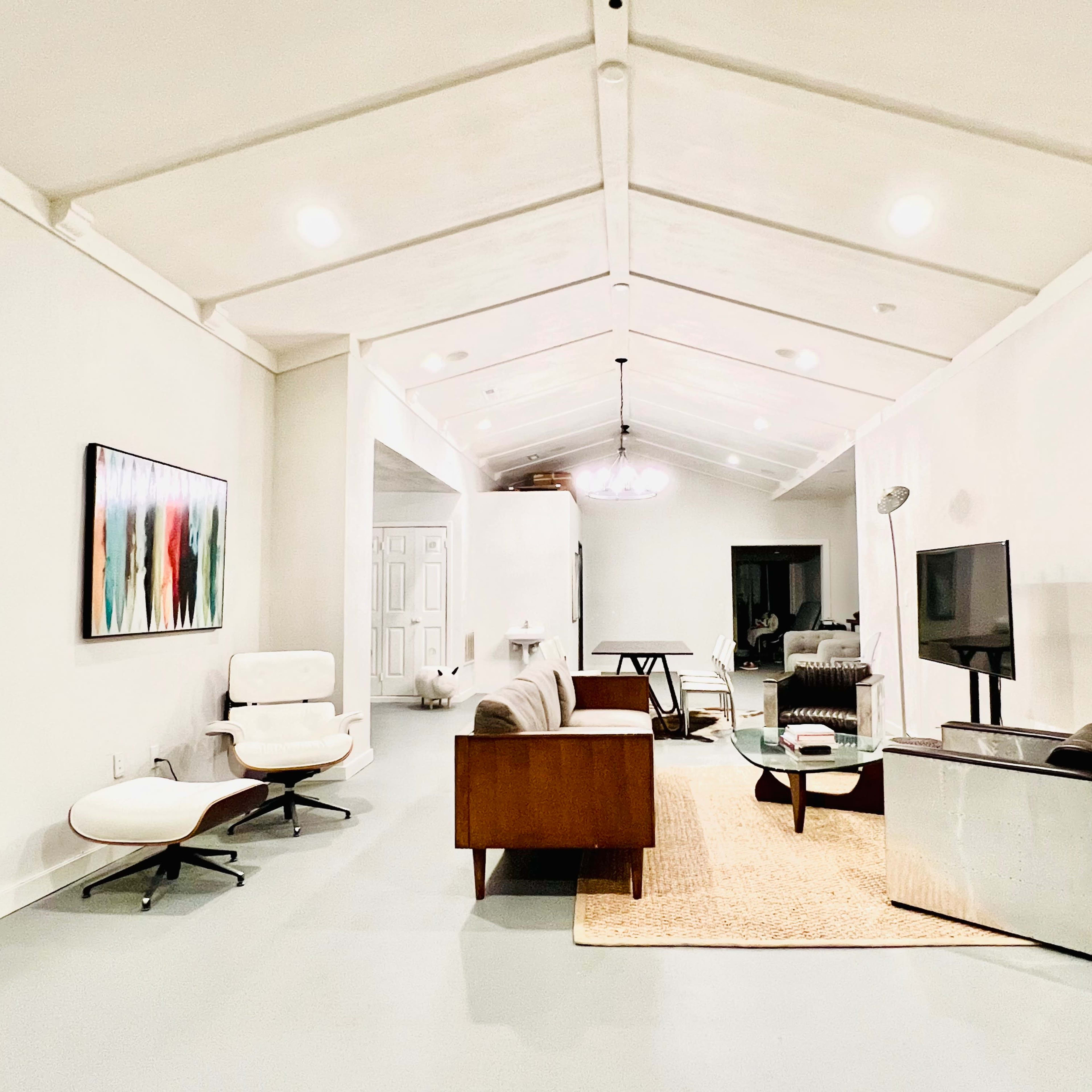 A modern, open living space featuring a seating area with a chair and sofa, a wooden coffee table, a television on a stand, and a large area rug.