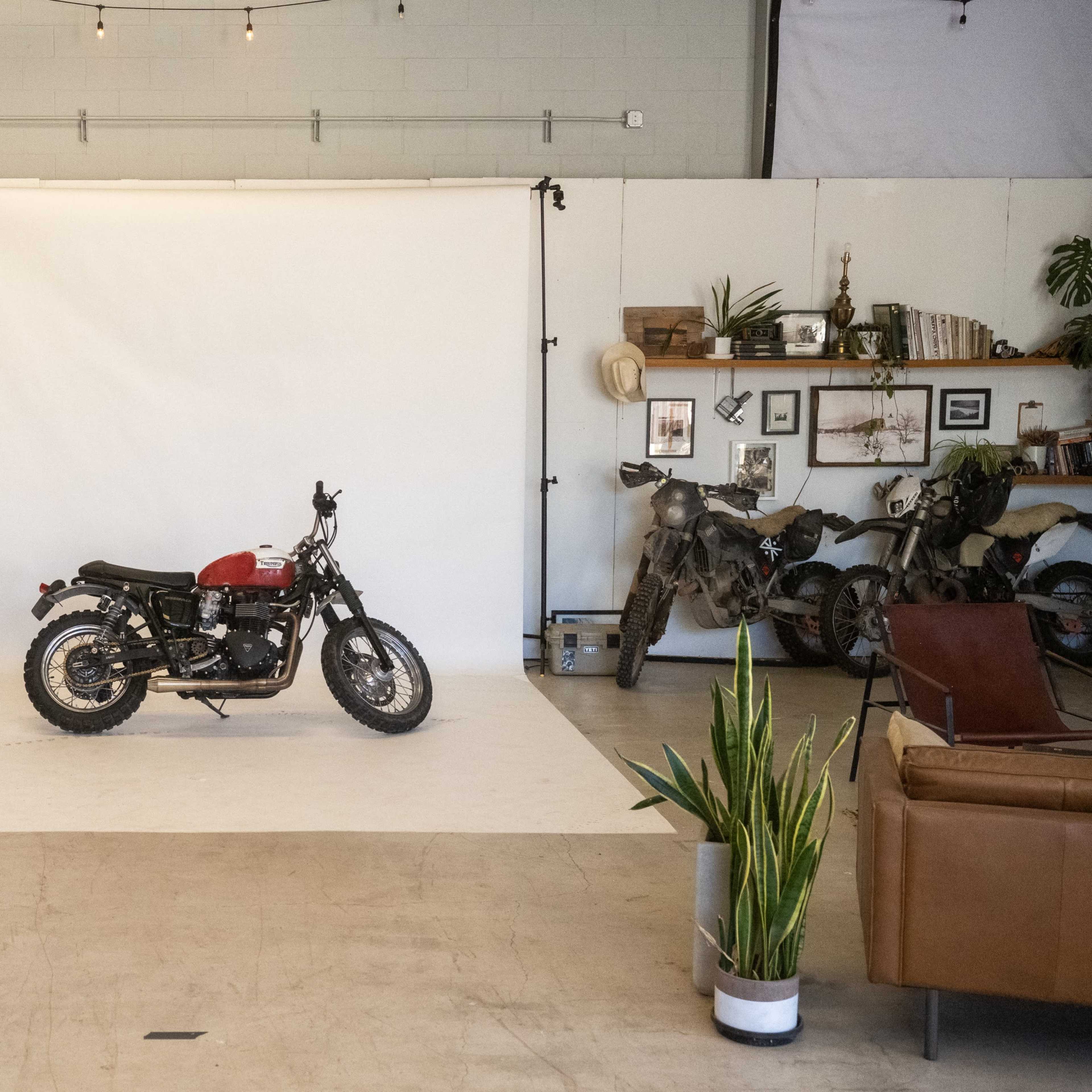 A motorcycle is positioned on a white backdrop in a spacious studio with various props and decor around the perimeter.