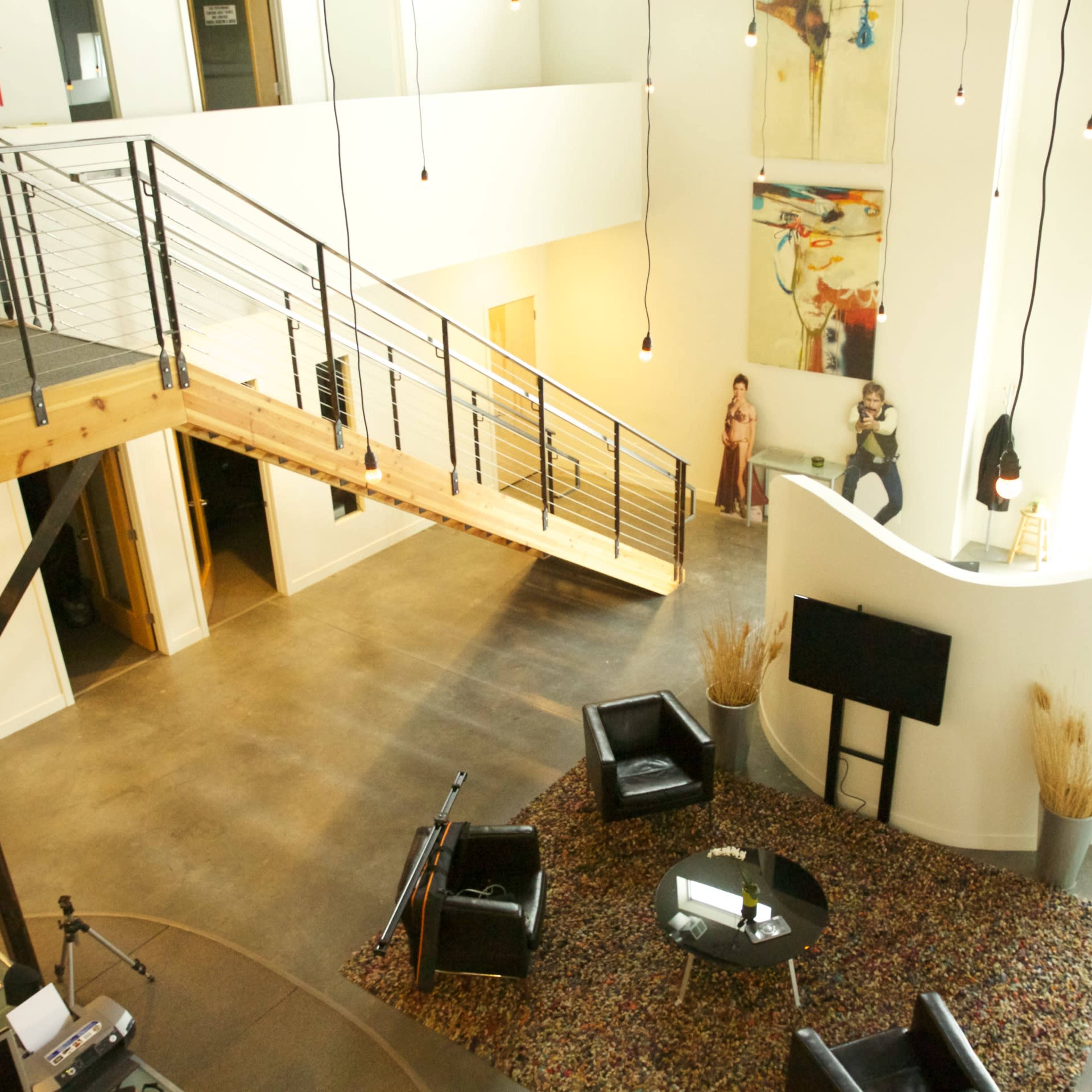 A spacious interior with a wooden staircase leading to an upper level, surrounded by modern decor, seating options, and artwork on the walls.