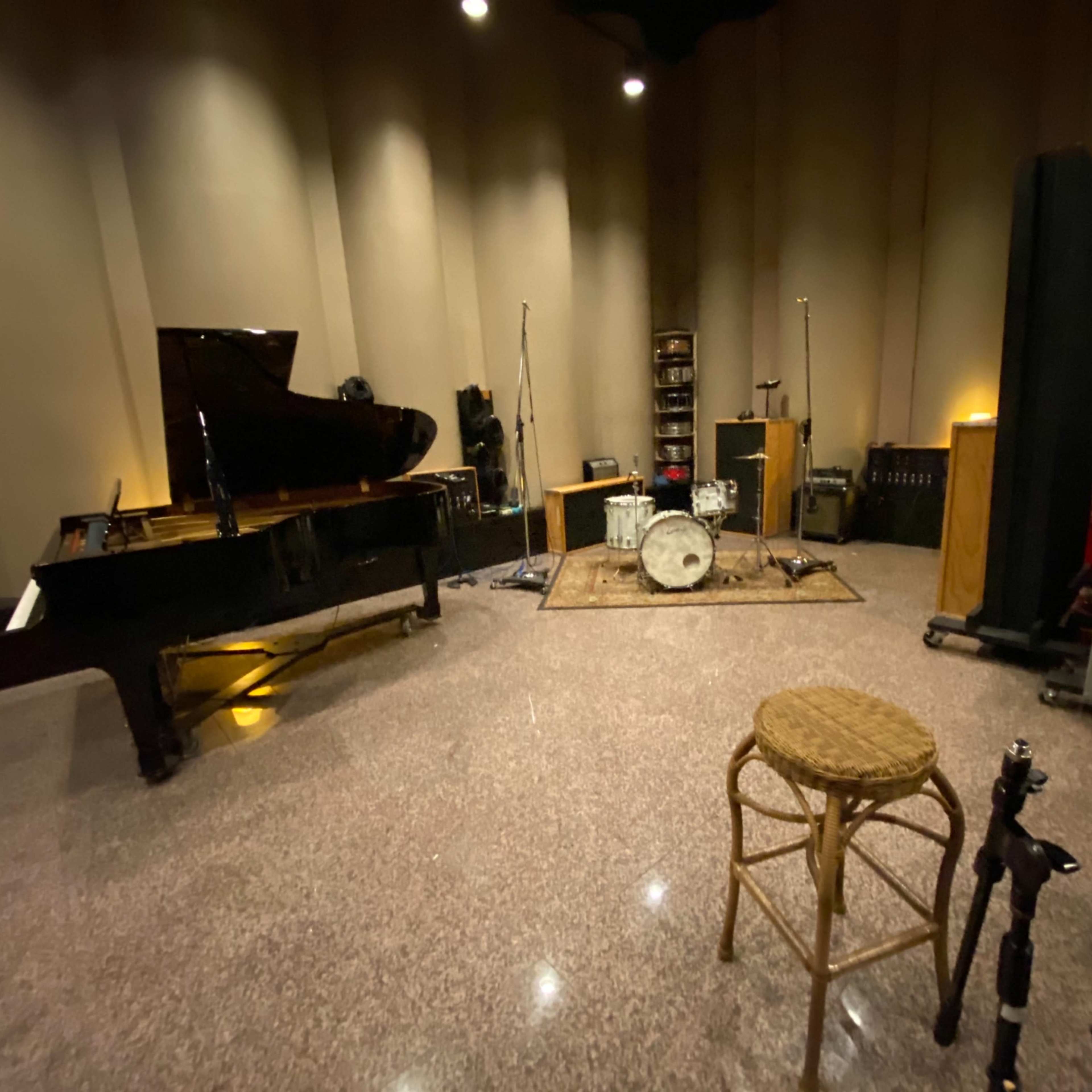A recording studio featuring a grand piano, a drum set, amplifiers, and a microphone stand.