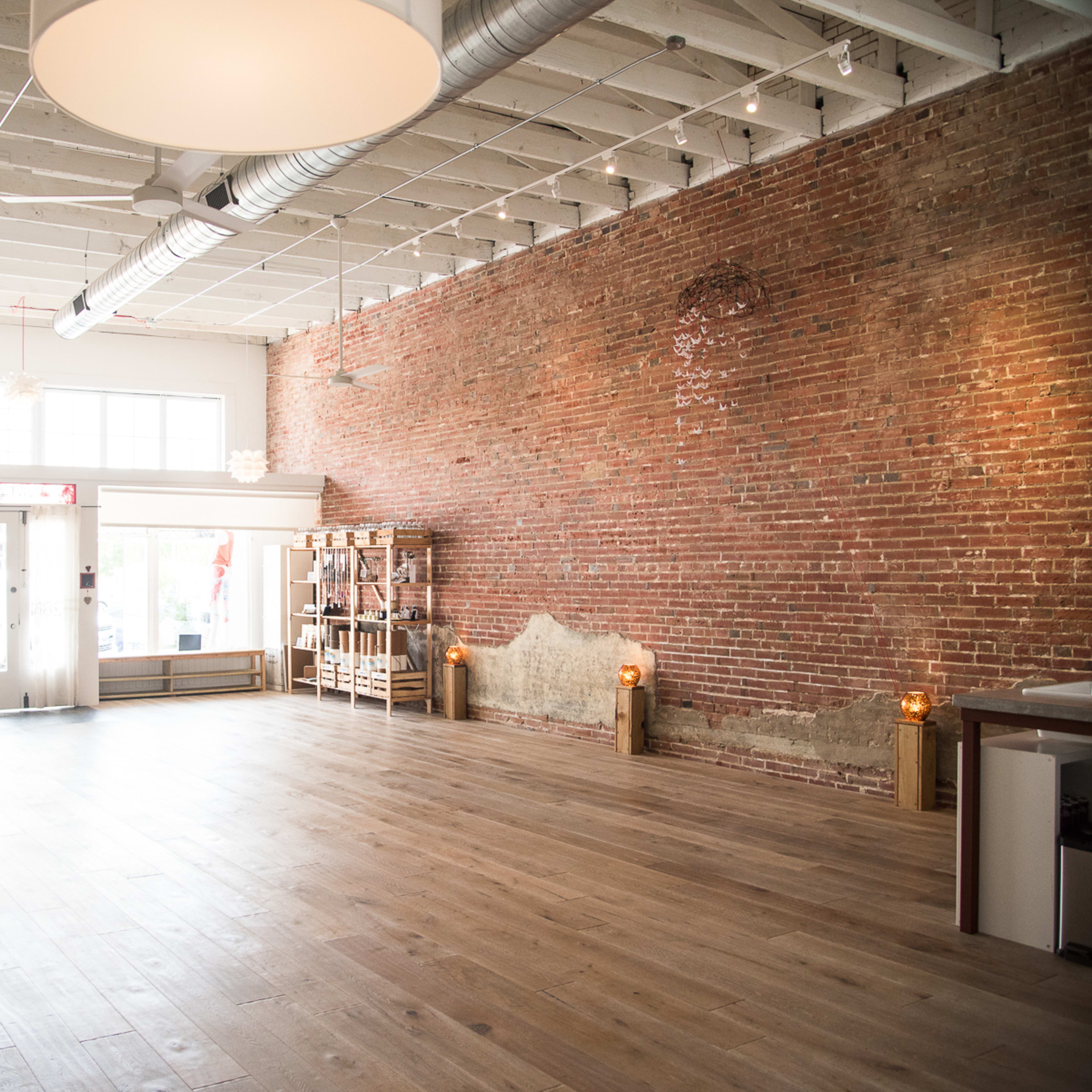A spacious, vacant interior with exposed brick walls, wooden flooring, and large windows letting in natural light.