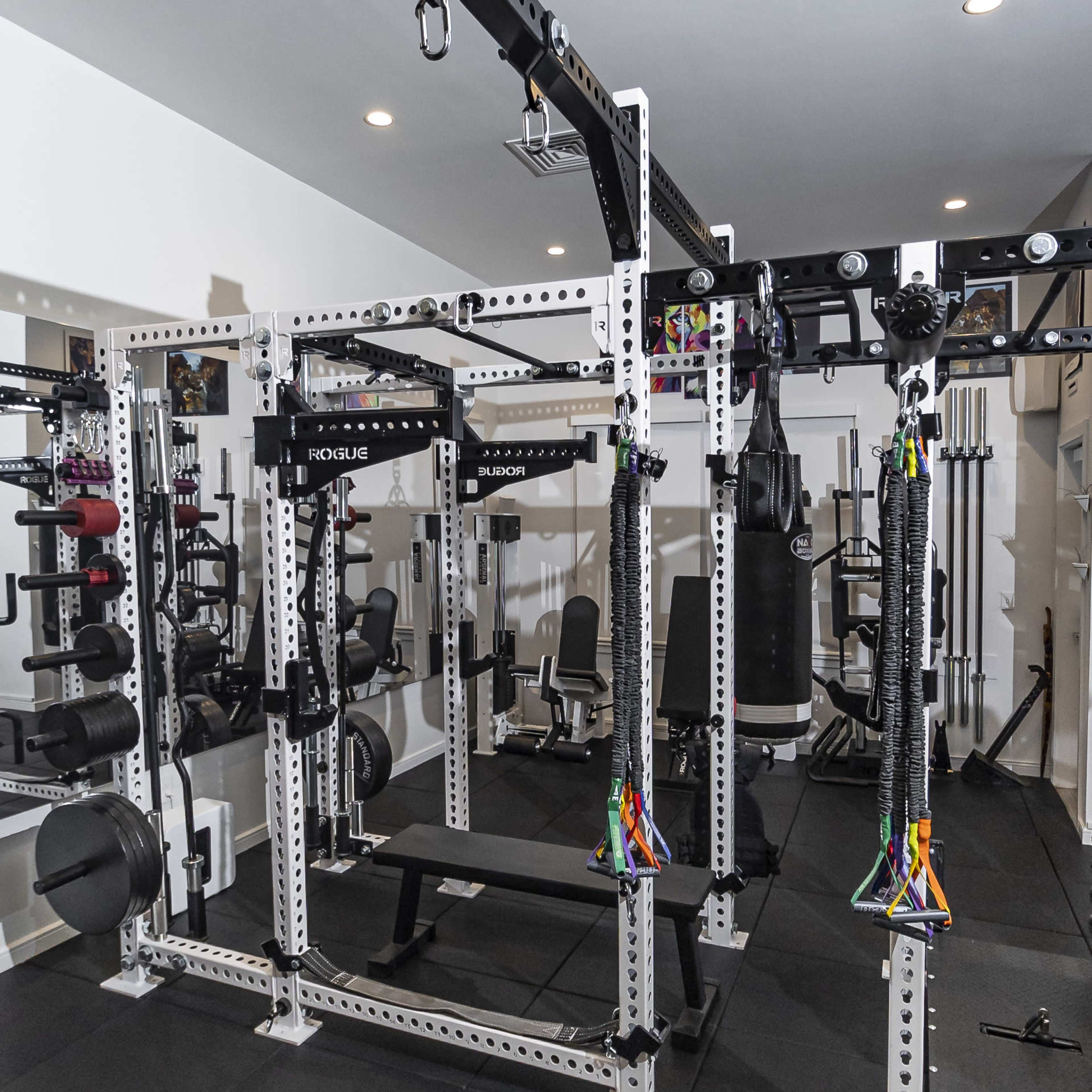 A well-equipped home gym featuring a multi-station weight rack, exercise machines, and various weights on a rubber flooring surface.