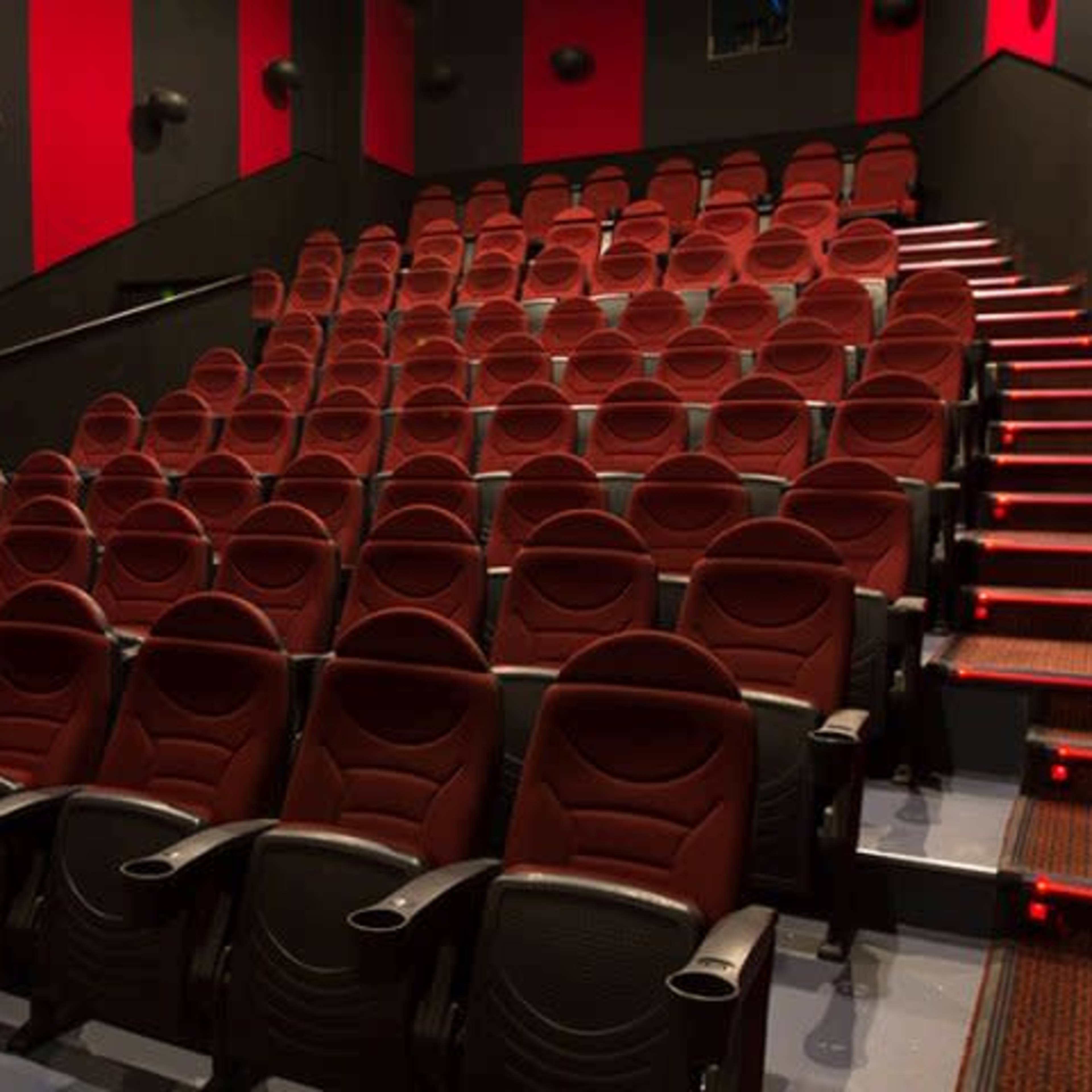 An empty movie theater with rows of red and black upholstered seats arranged in a stepped formation.