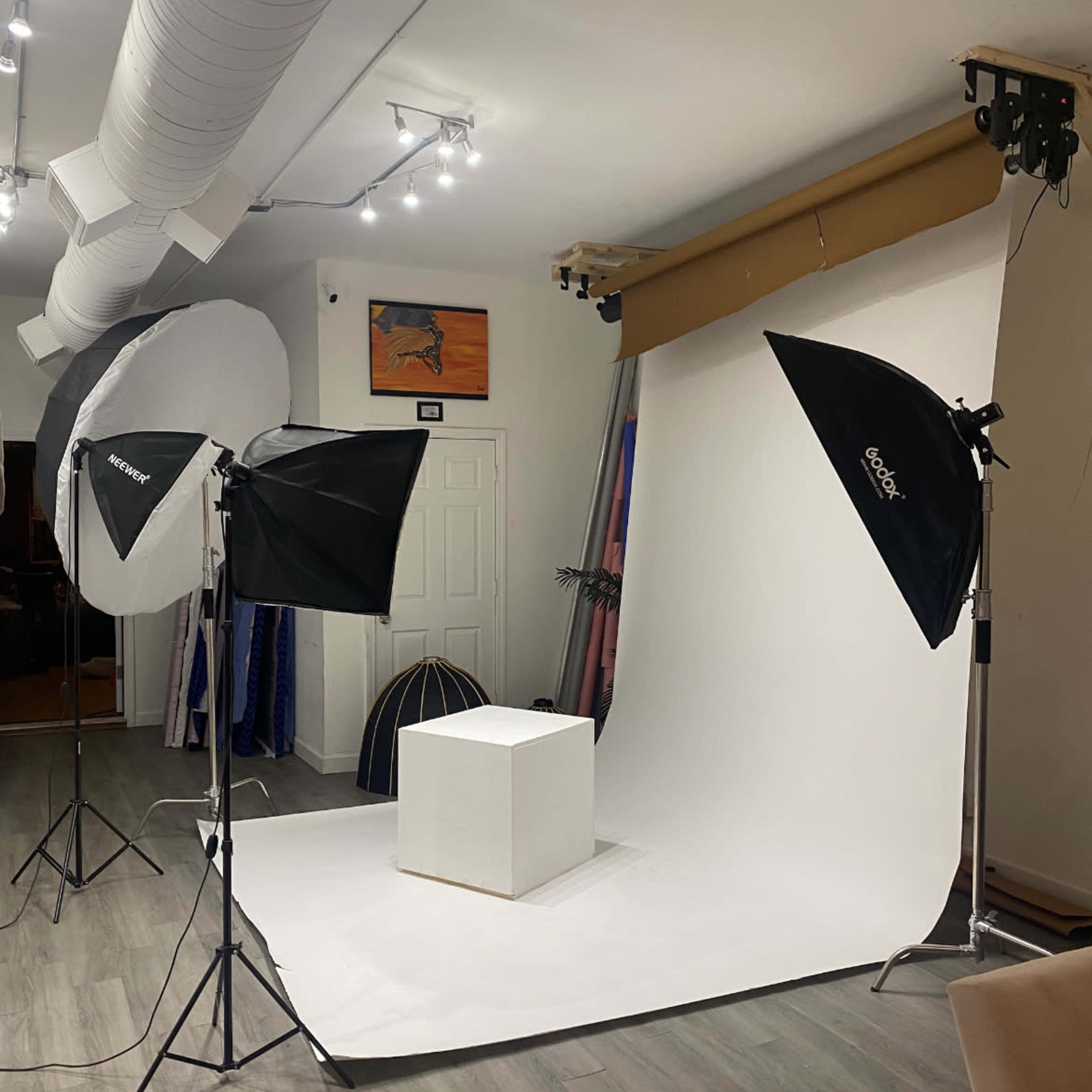 A photography studio setup with softbox lights and a plain white backdrop featuring an empty pedestal in the center.