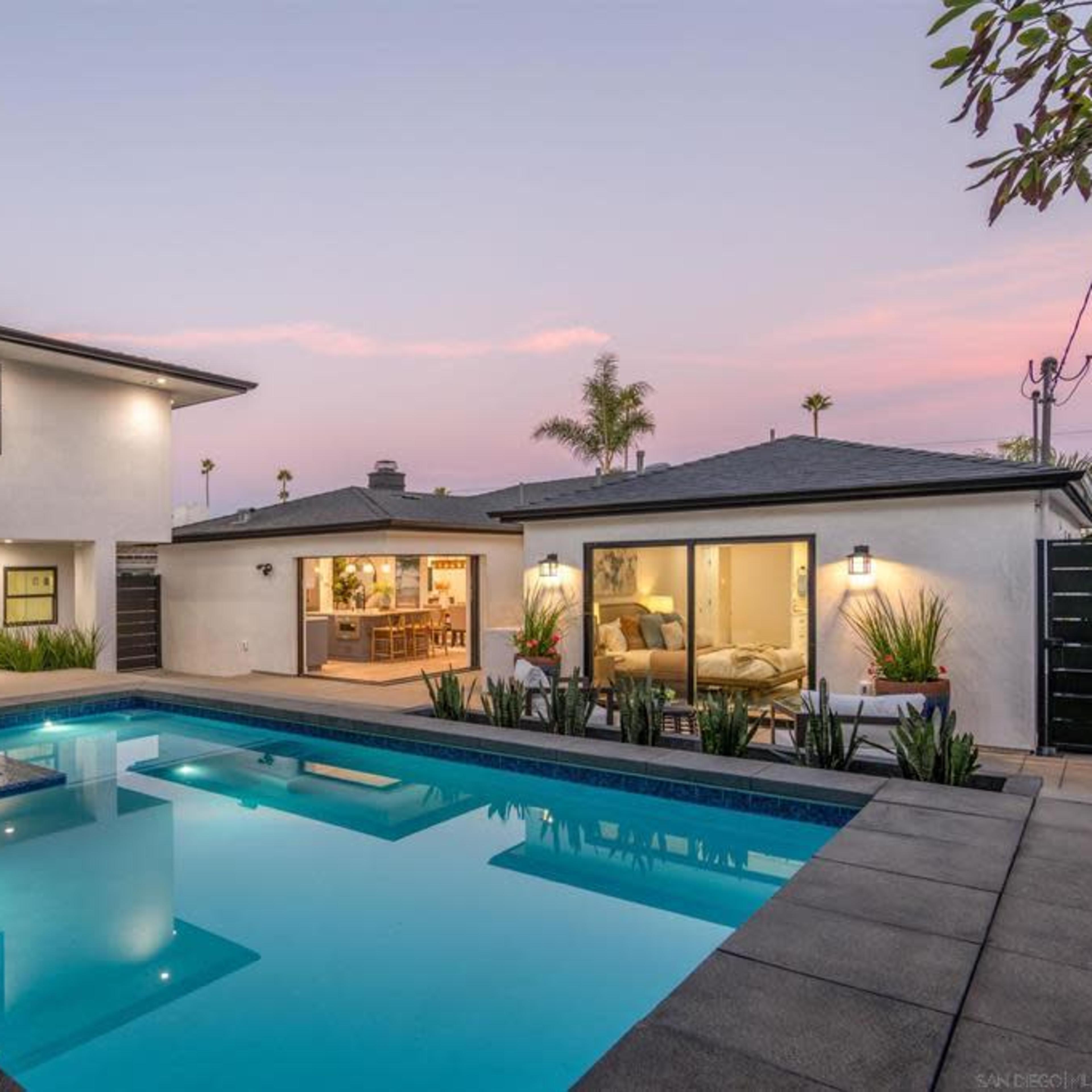 A modern two-story home with a pool and spa is surrounded by landscaped greenery and has a patio area for outdoor relaxation.