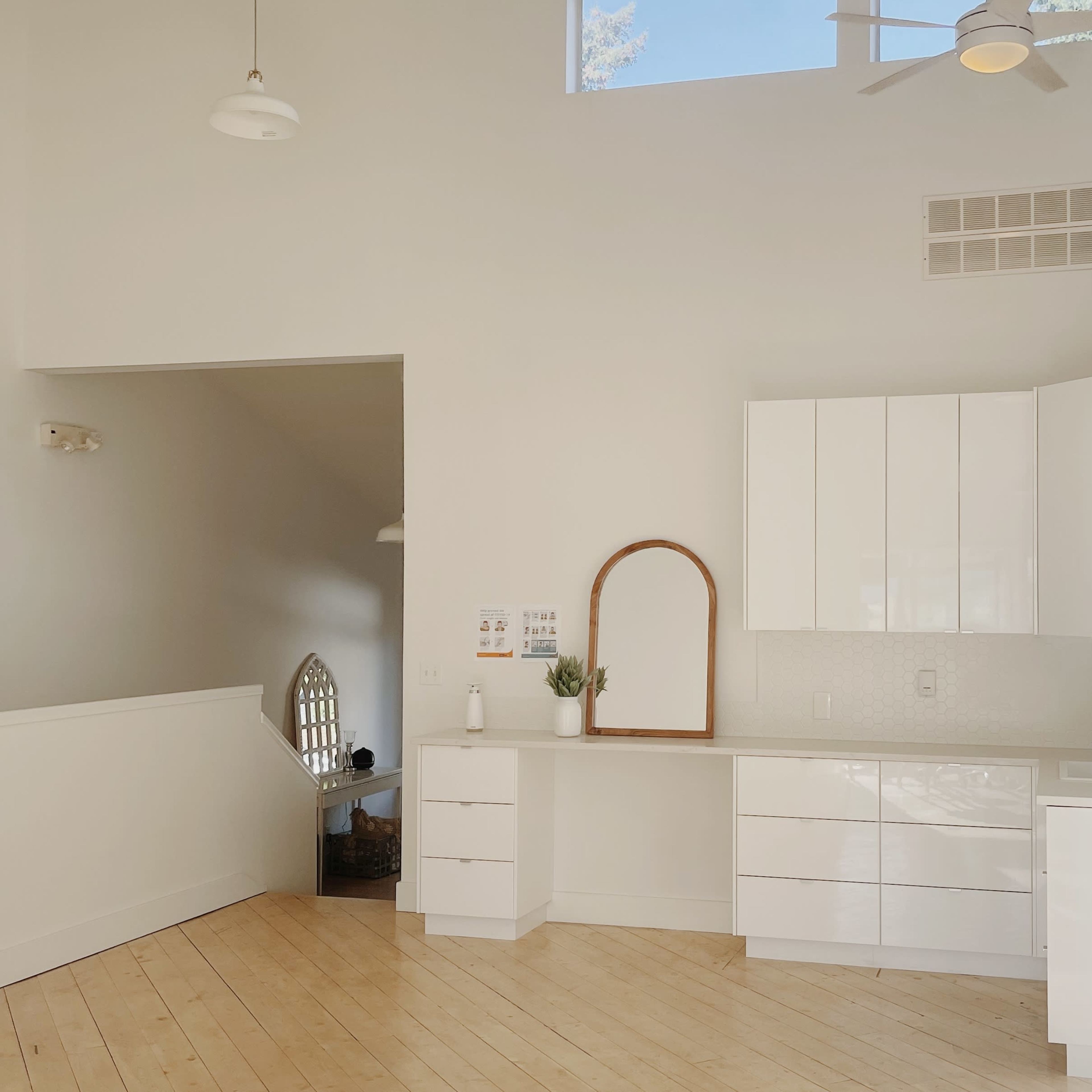 A modern kitchen with white cabinetry, a sink, and a large mirror above a counter, adjacent to an open living space with a staircase.