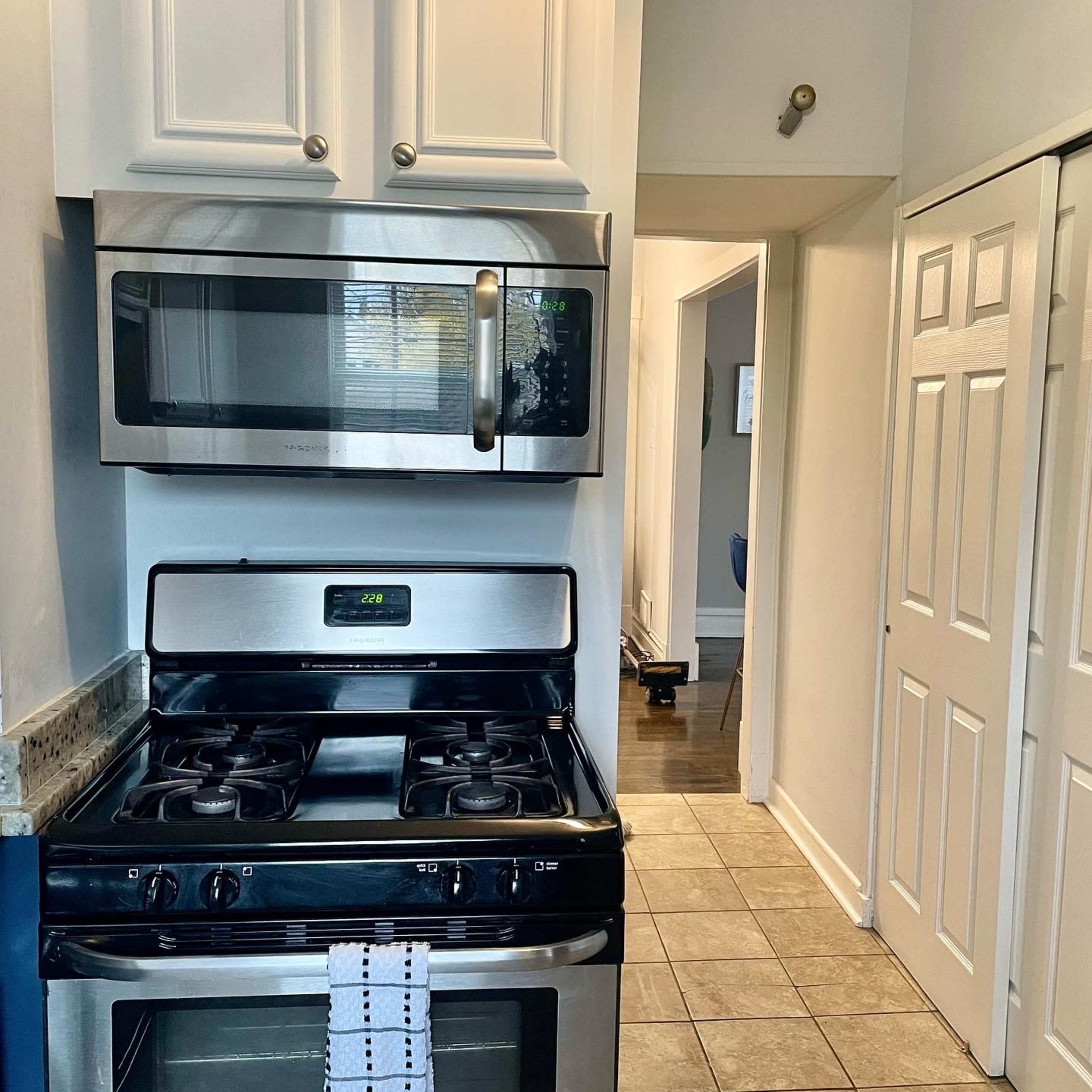 A kitchen featuring a stainless steel microwave and gas stove, with white cabinets and tiled flooring.