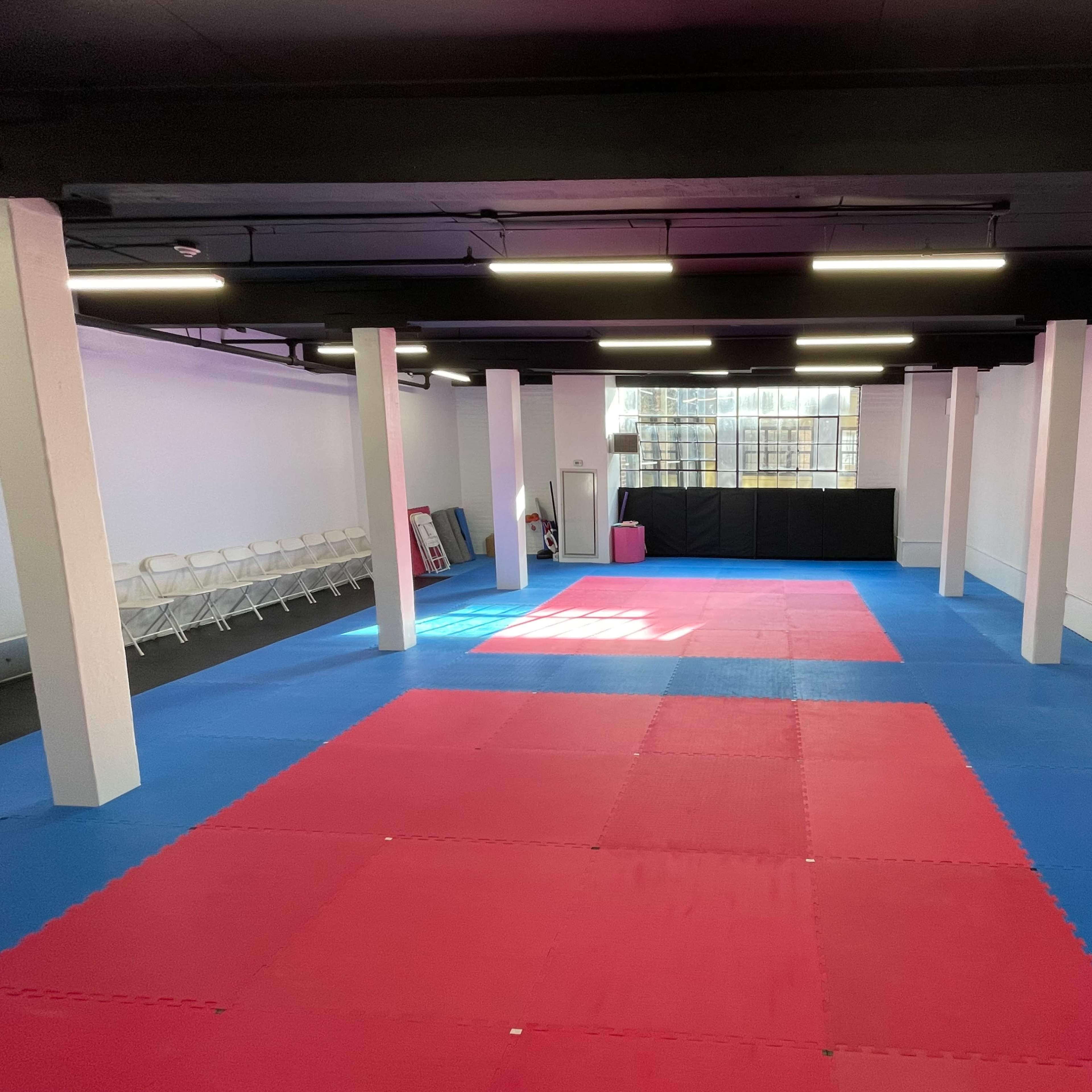 A spacious training room with red and blue mats, white pillars, and a row of chairs along one wall.