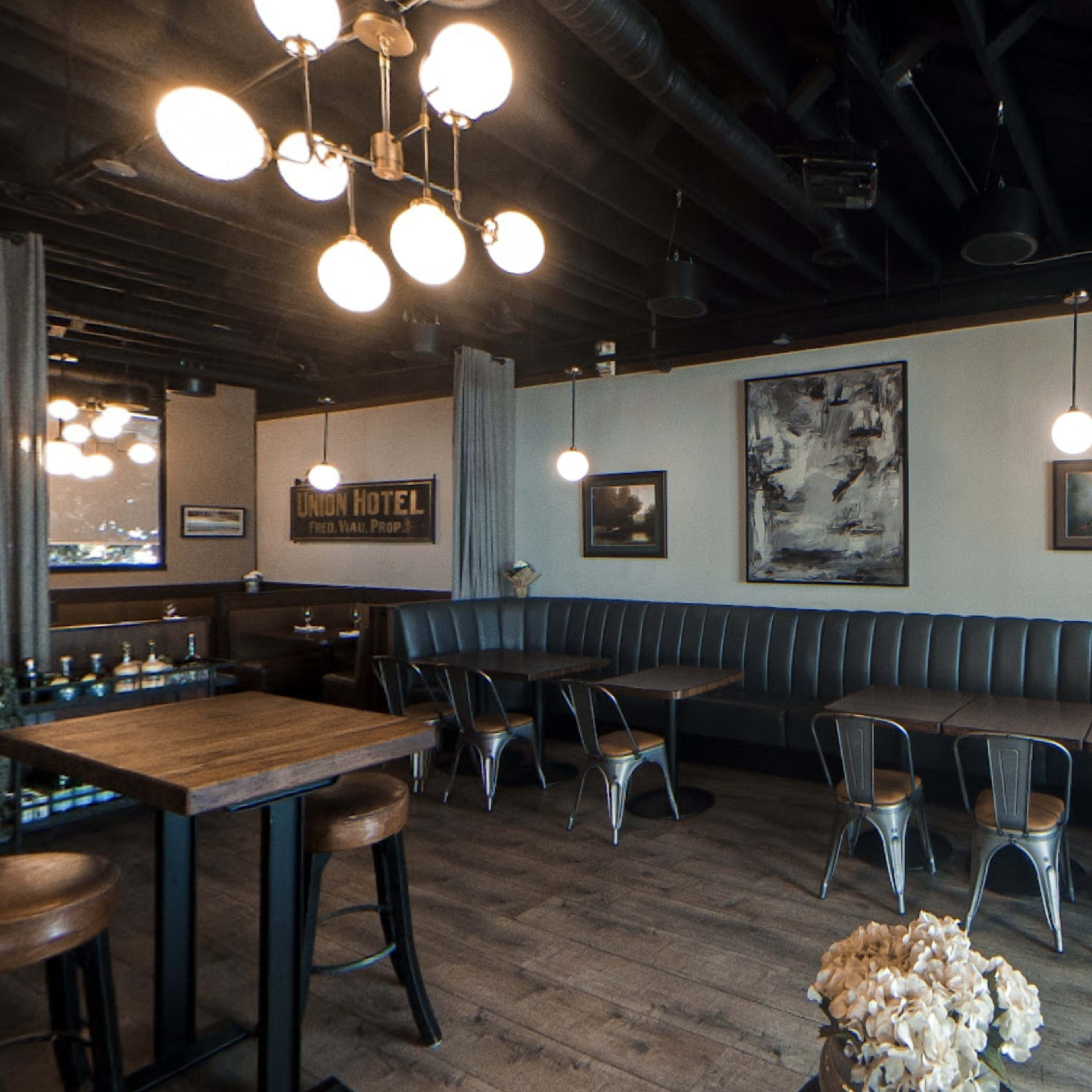 A modern café interior with a curved leather booth, wooden tables, and various artwork on the walls, illuminated by hanging light fixtures.