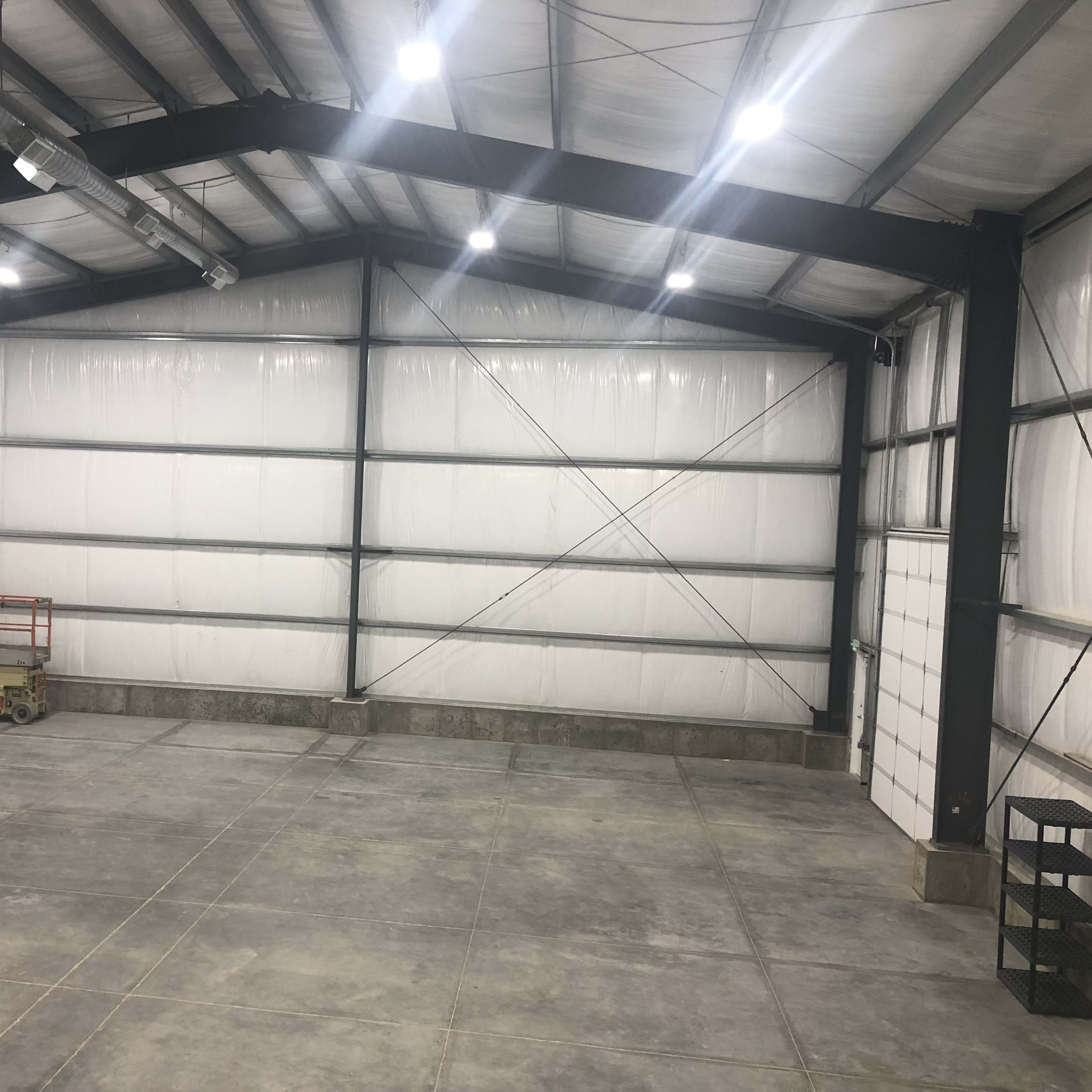The interior of a large industrial warehouse with white walls, concrete flooring, and high ceilings supported by metal beams.