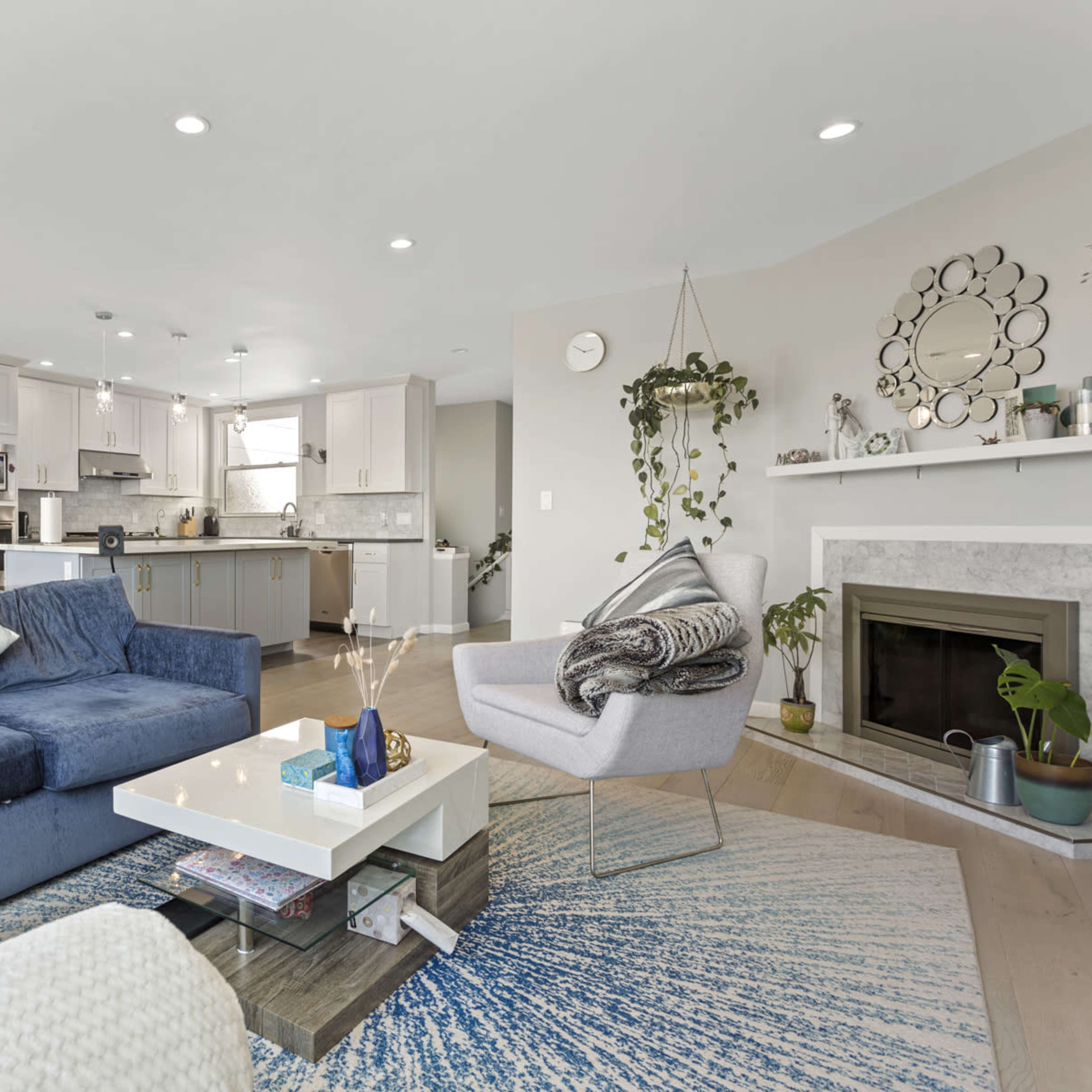 A modern living space features a blue sectional sofa, a coffee table, and a well-equipped kitchen with light-colored cabinets and a dining area.