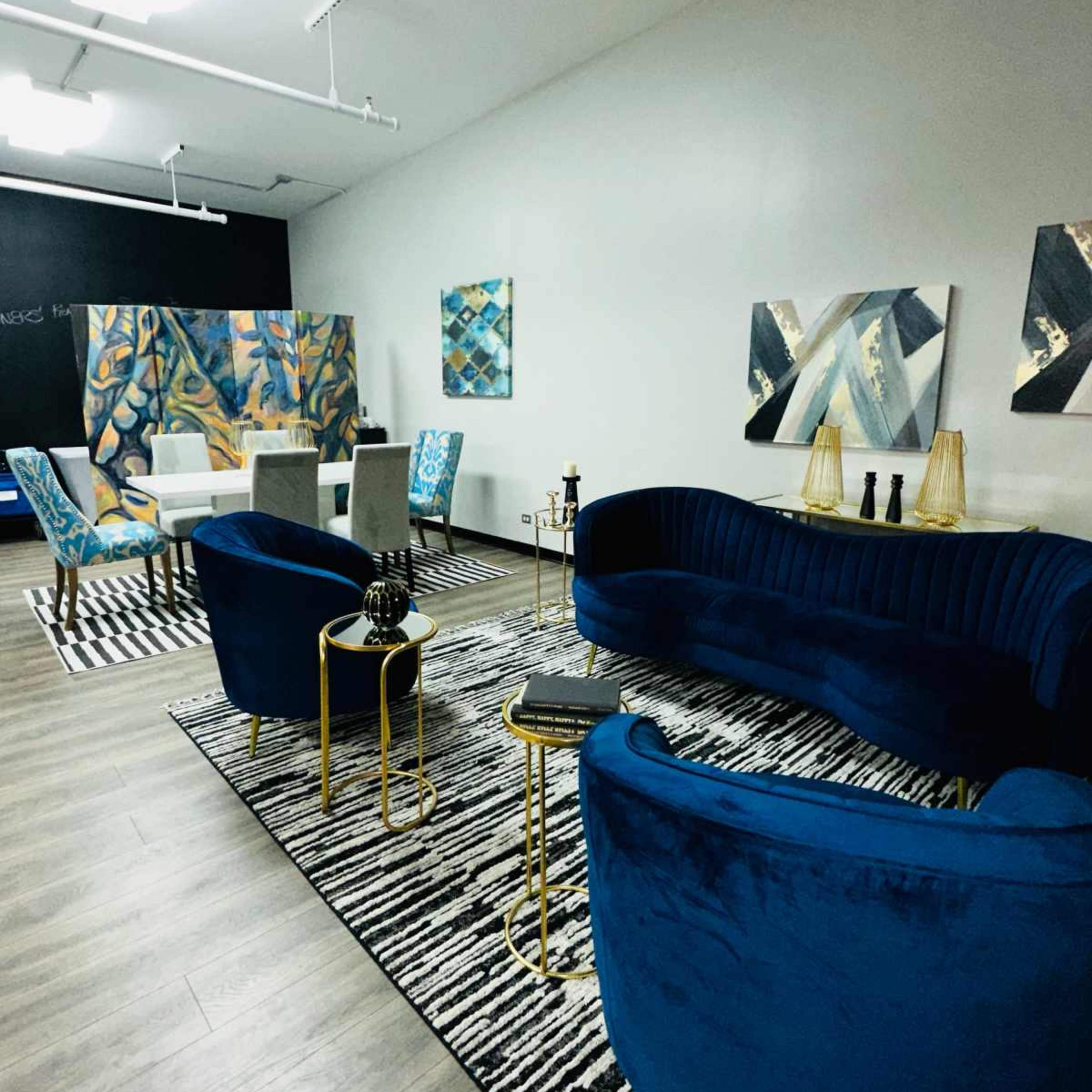 A modern lounge area with blue velvet sofas, gold accents, and abstract artwork on the walls, complemented by a striped area rug.
